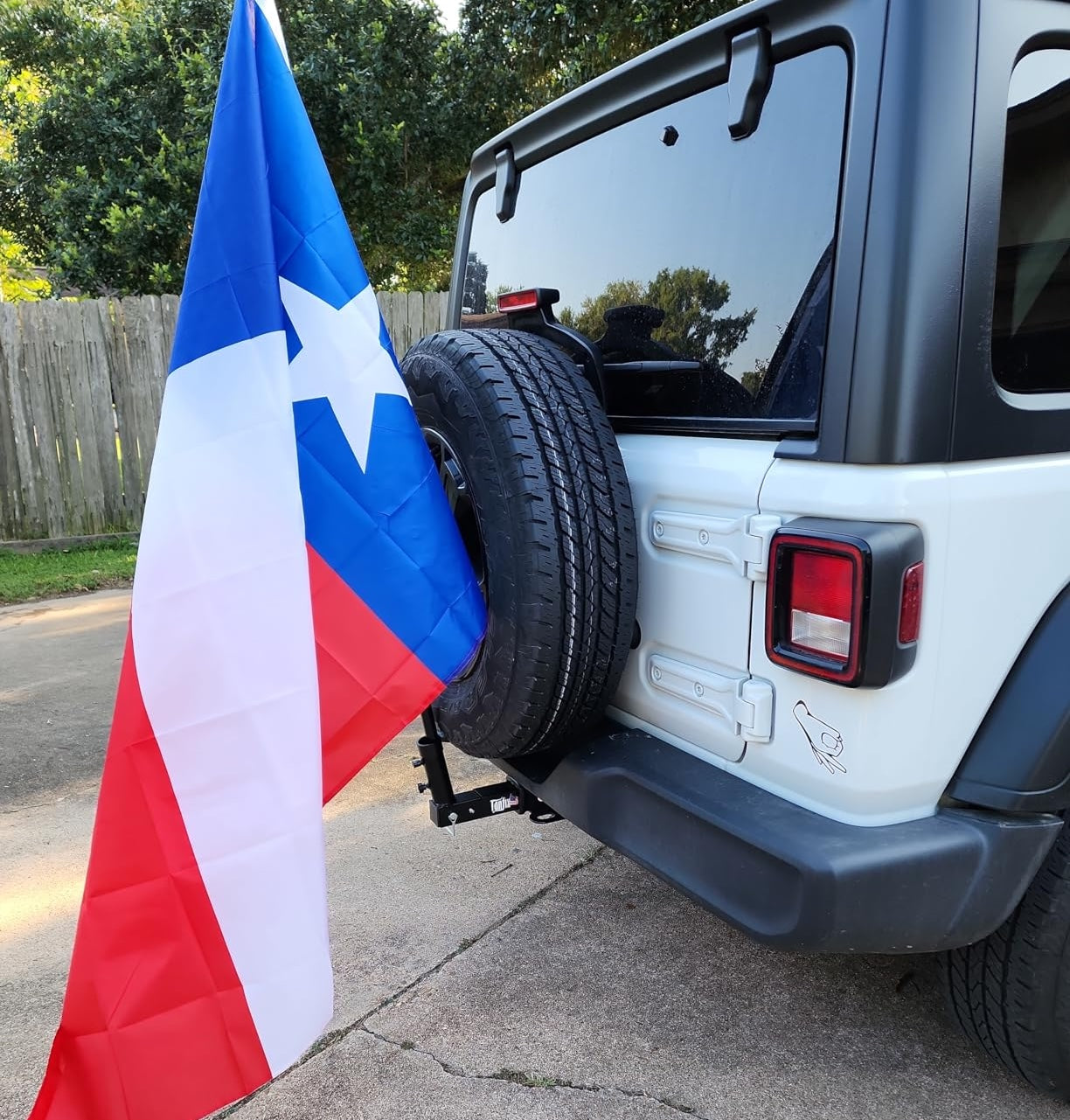 White Jeep Wrangler with a flag pole hitch receiver holding a flag with red, white, and blue colors.
