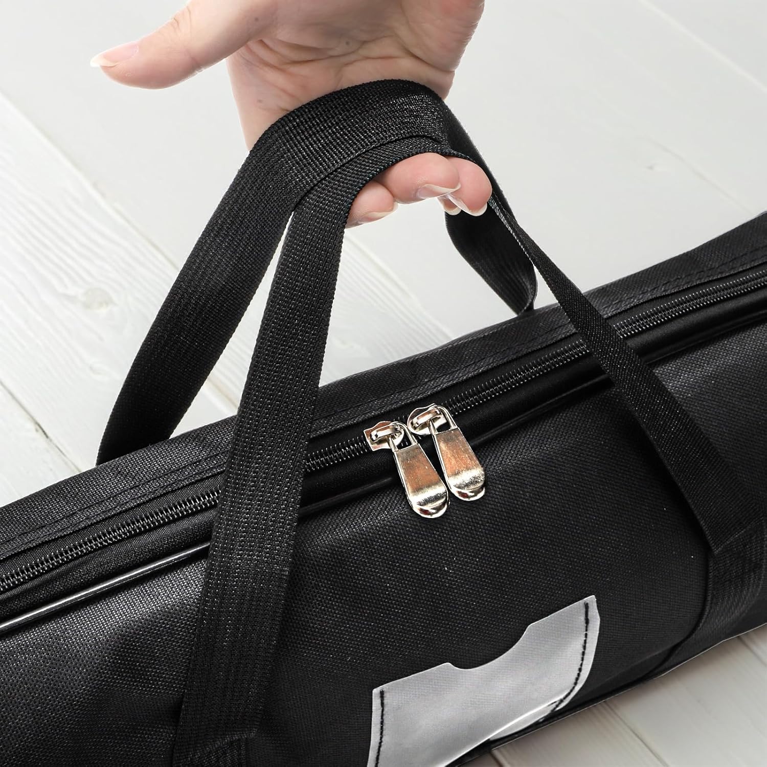 Black feather flag bag with a handle being held by a hand on a light wooden floor.
