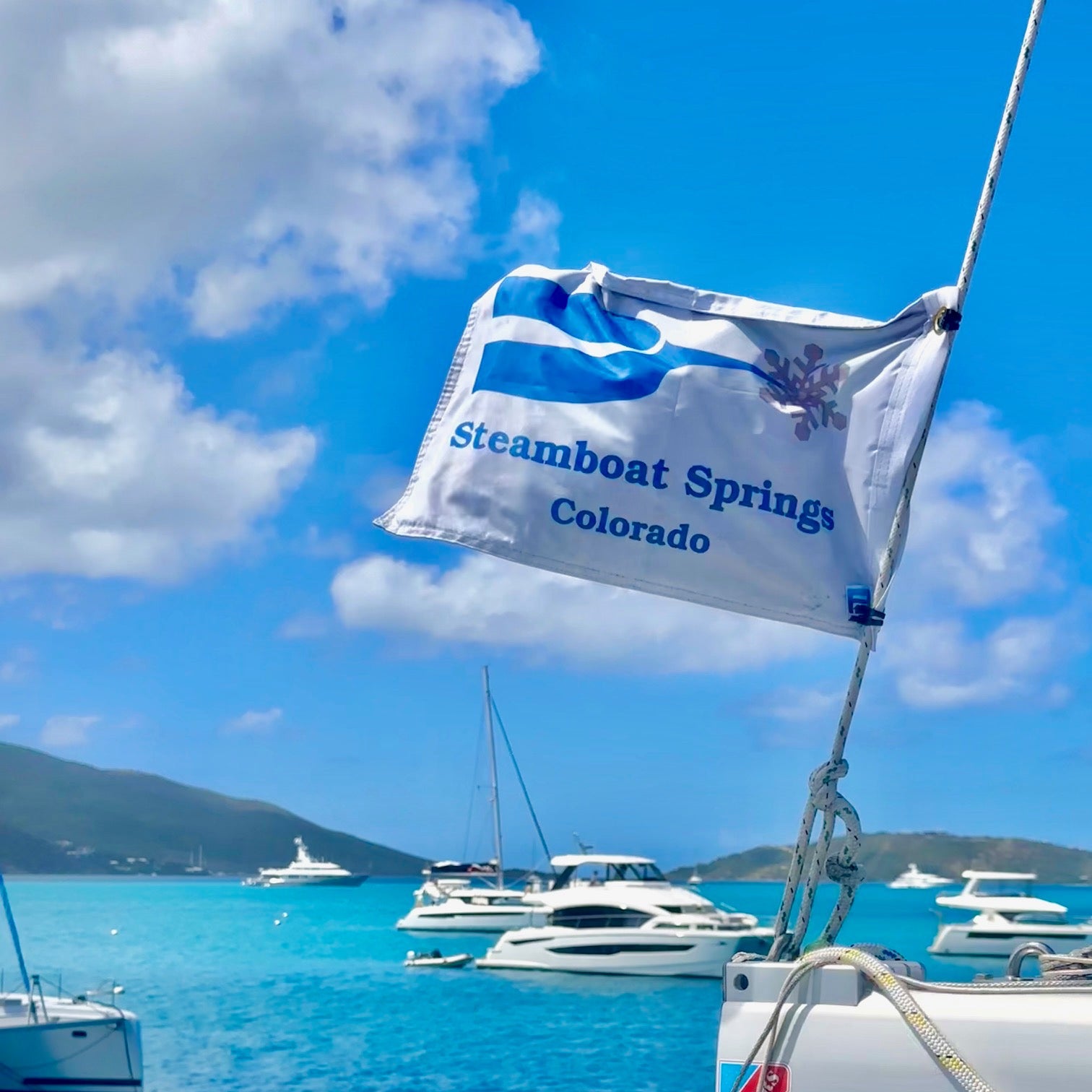 Yacht with a Steamboat Springs, Colorado flag against a blue sky and turquoise water.