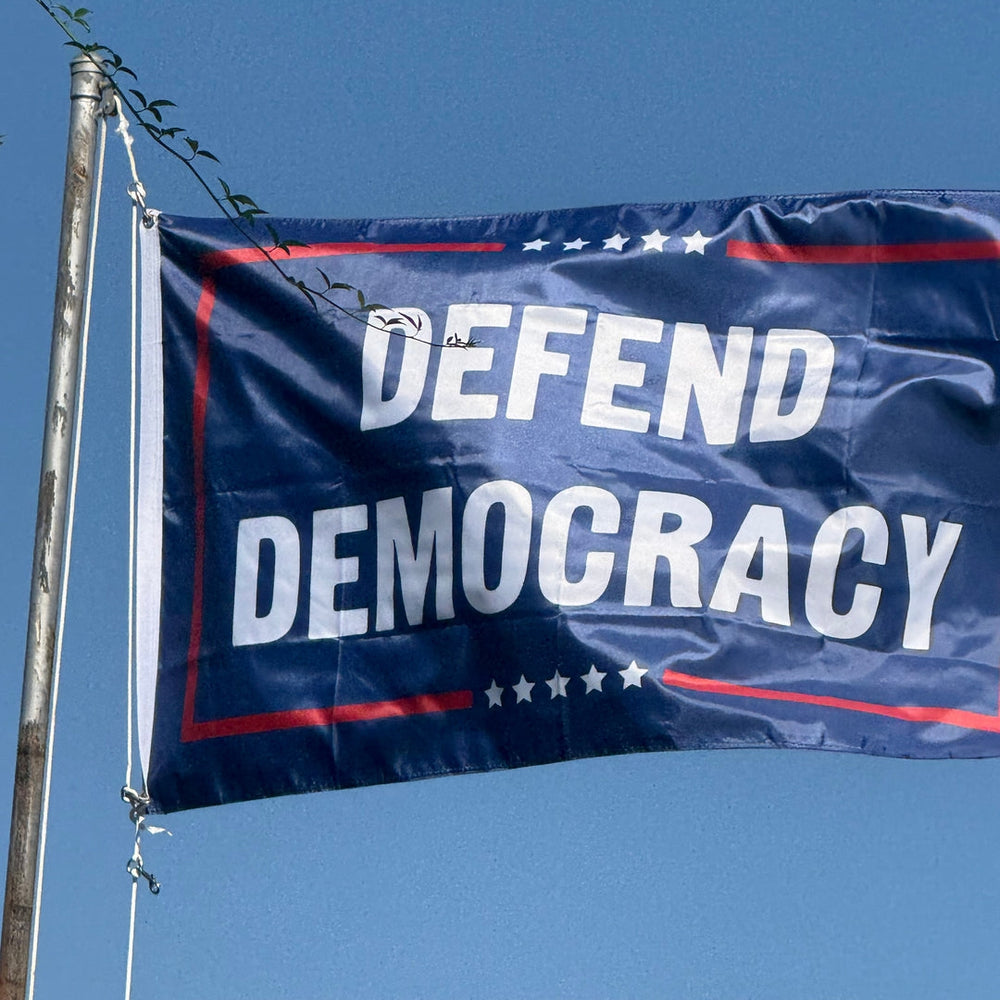 Flag with 'DEFEND DEMOCRACY' text against a clear blue sky