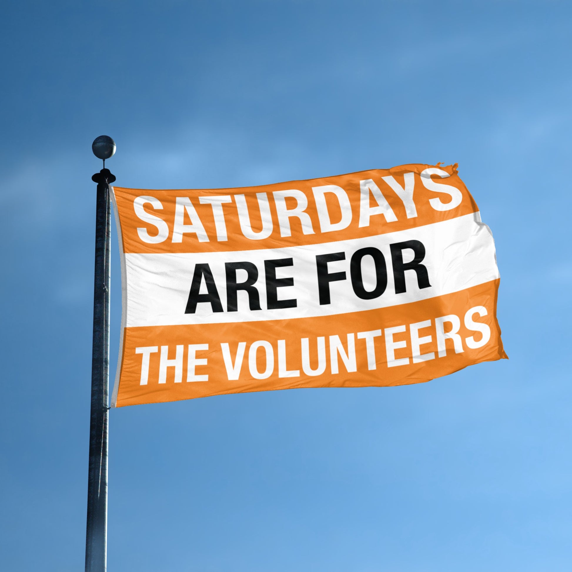 Flag with 'Saturdays are for the volunteers' text against a blue sky