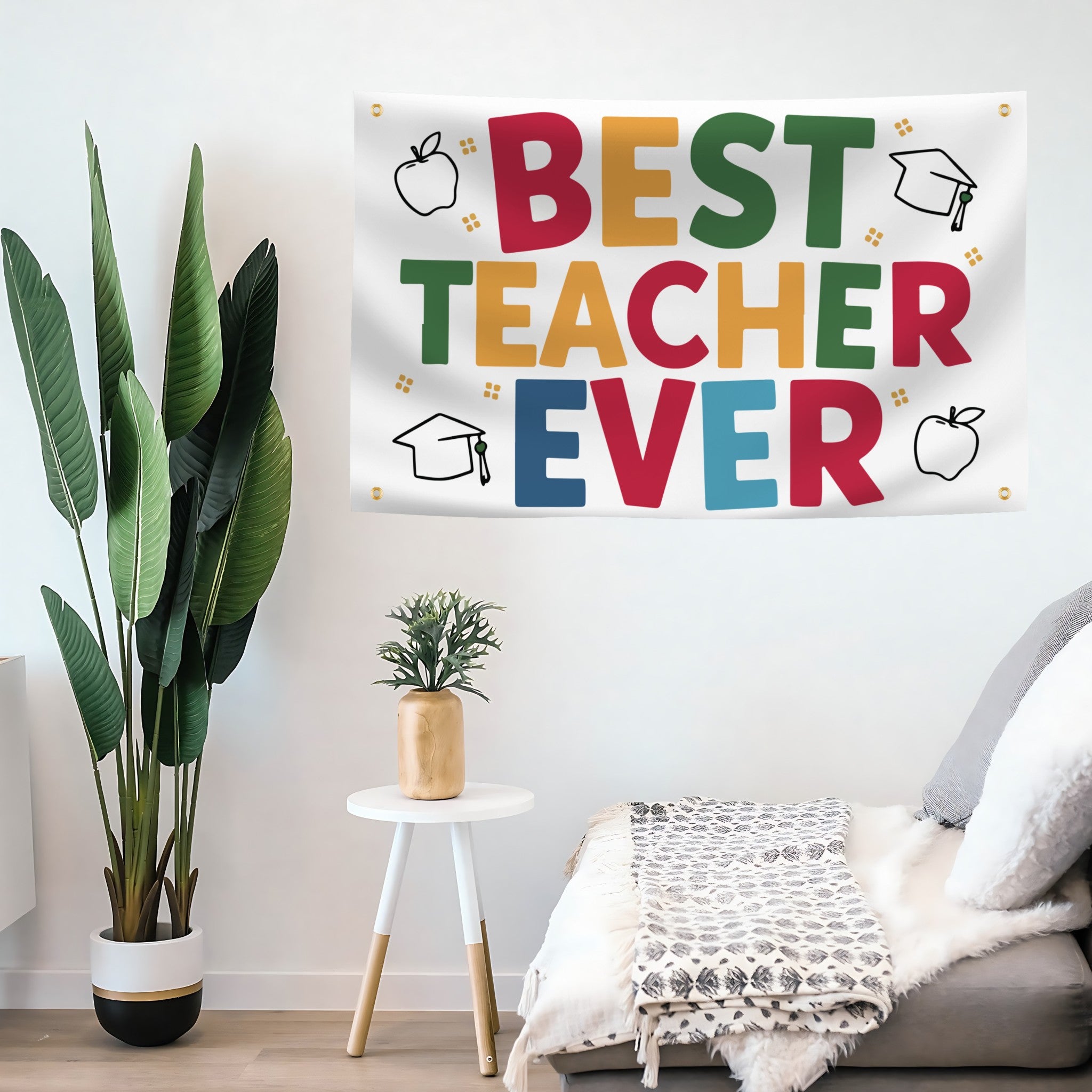 A colorful 'BEST TEACHER EVER' banner displayed in a styled room setting with a potted plant, a small side table, and a sofa.
