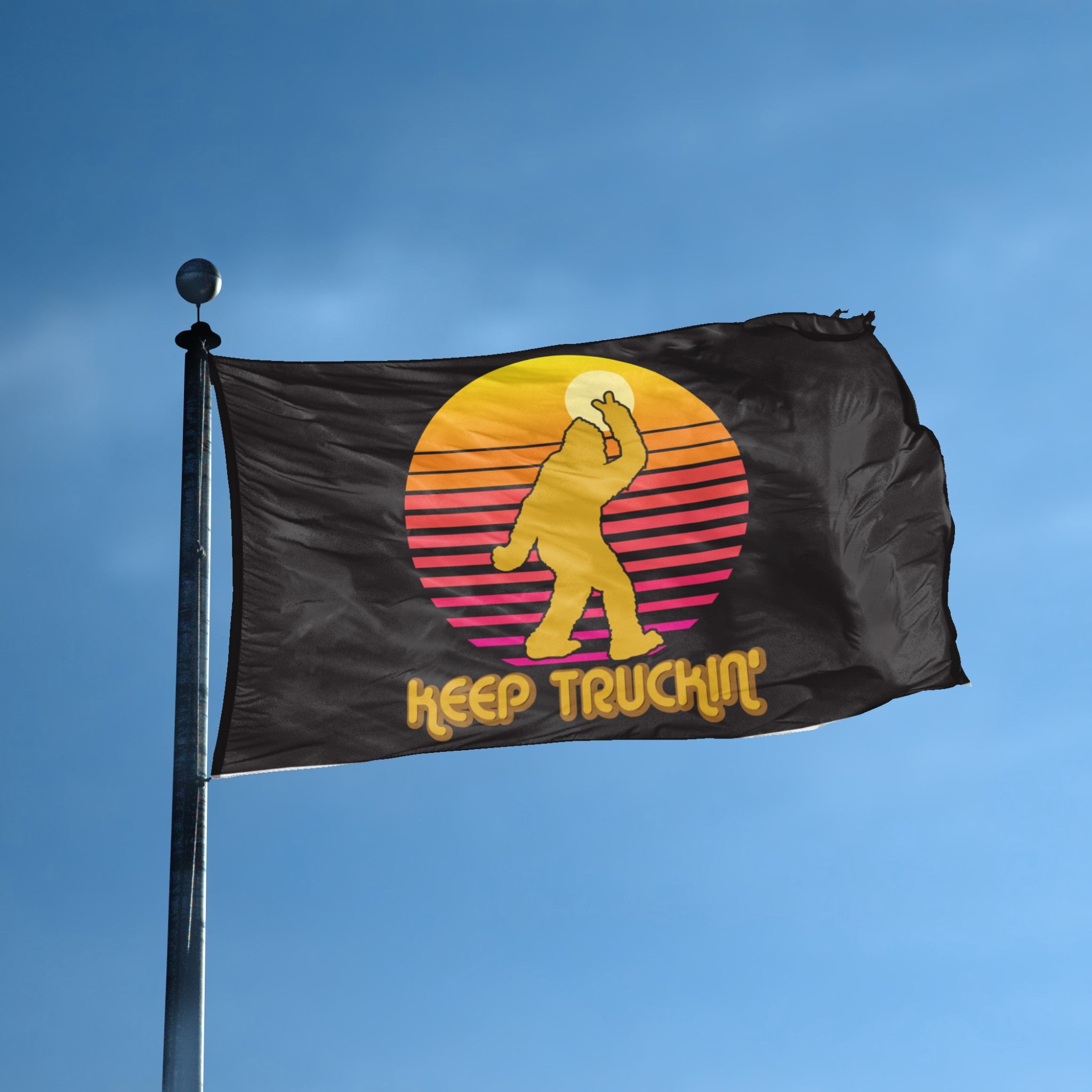 A flag with the theme "Bigfoot Keep Truckin'" displayed on a tall flag pole and blue skies.
