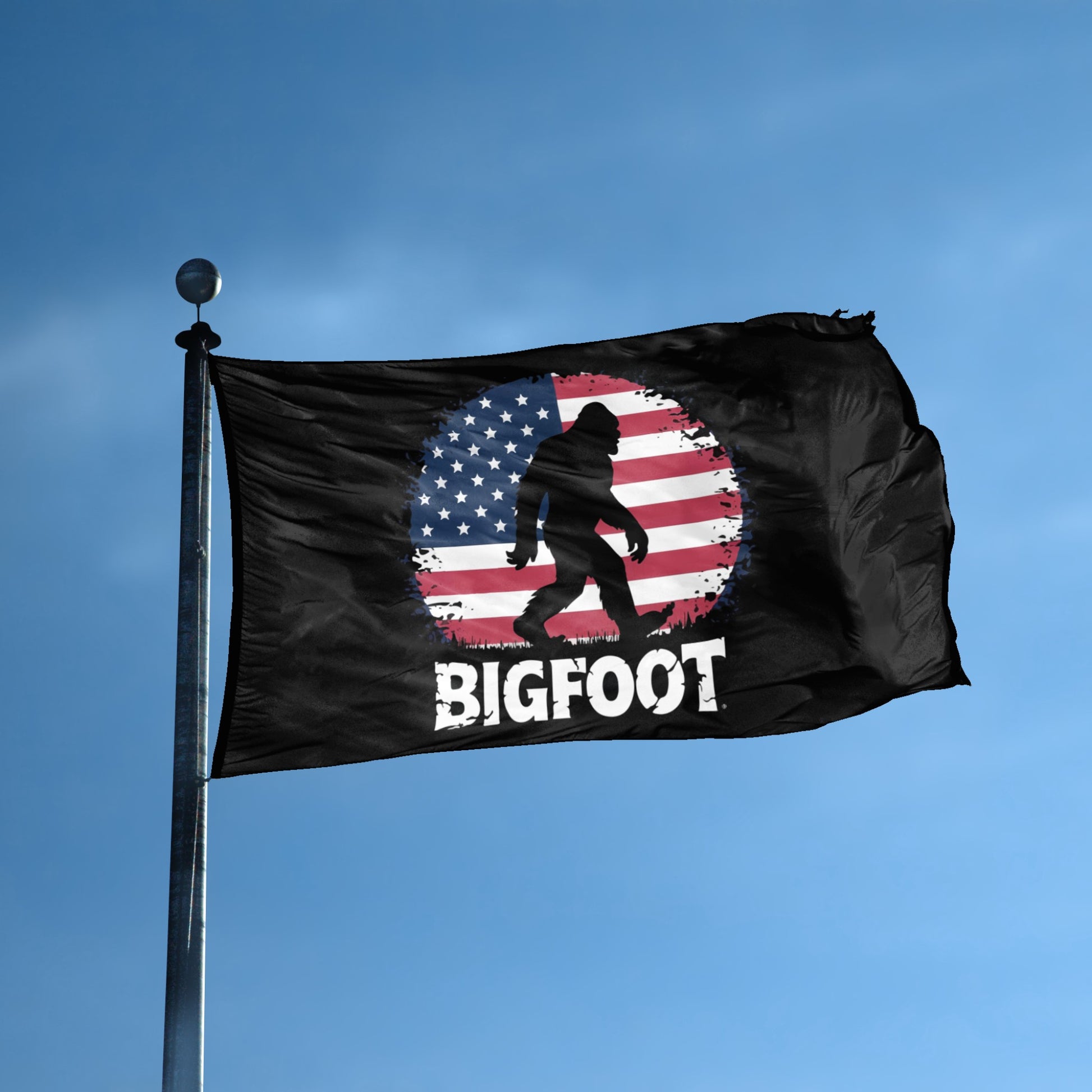 A flag with the theme "Bigfoot Patriotic" displayed on a tall flag pole and blue skies.