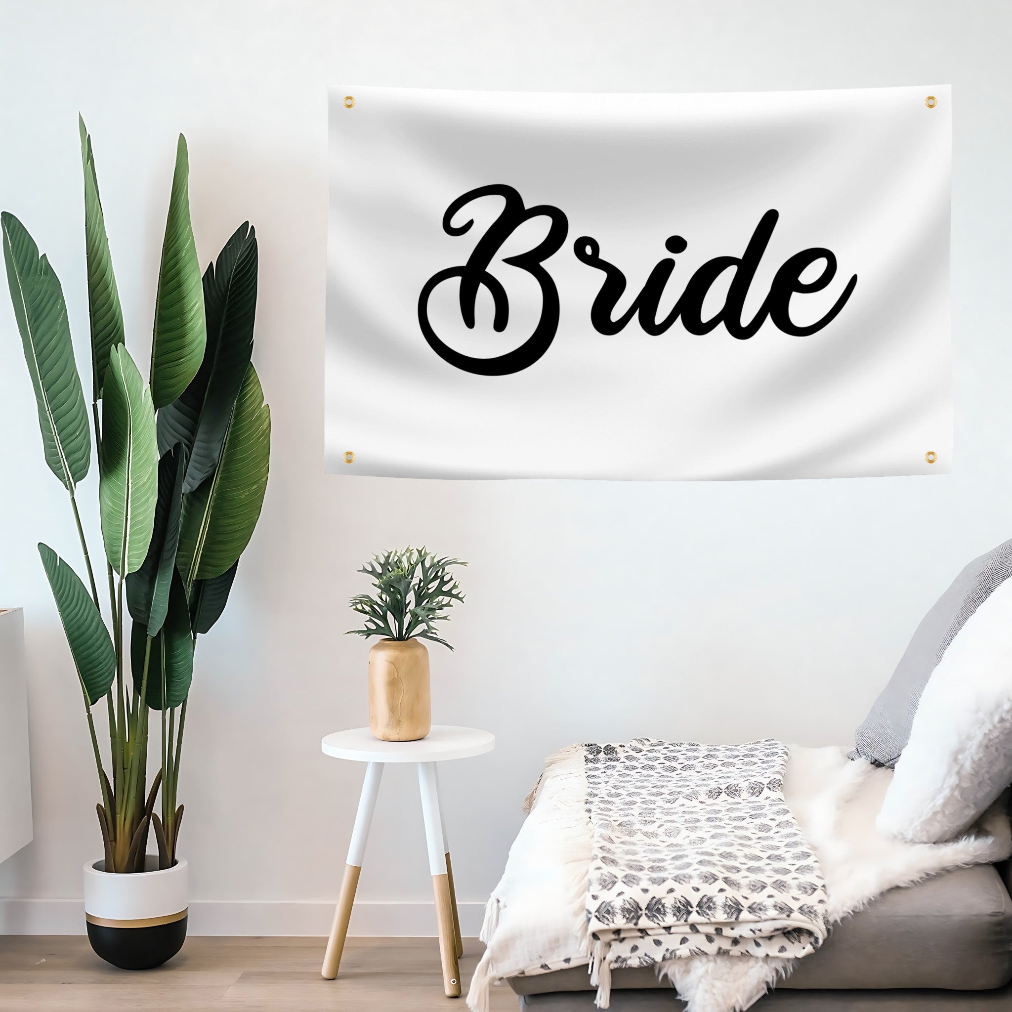 White wall with 'Bride' flag banner, potted plant, and small table with decorative items.
