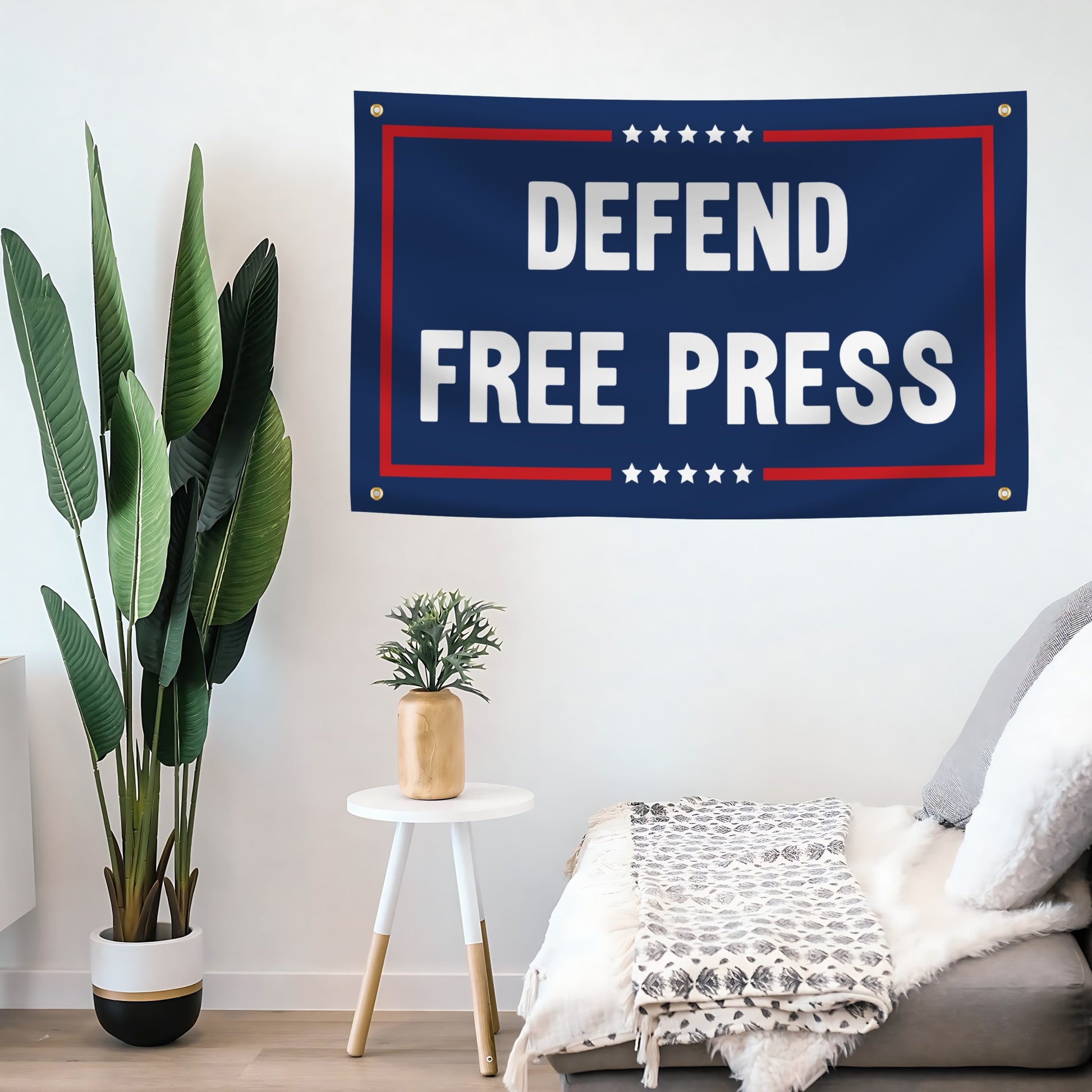 Banner with 'Defend Free Press' text hanging on a wall in a room with plants and furniture.