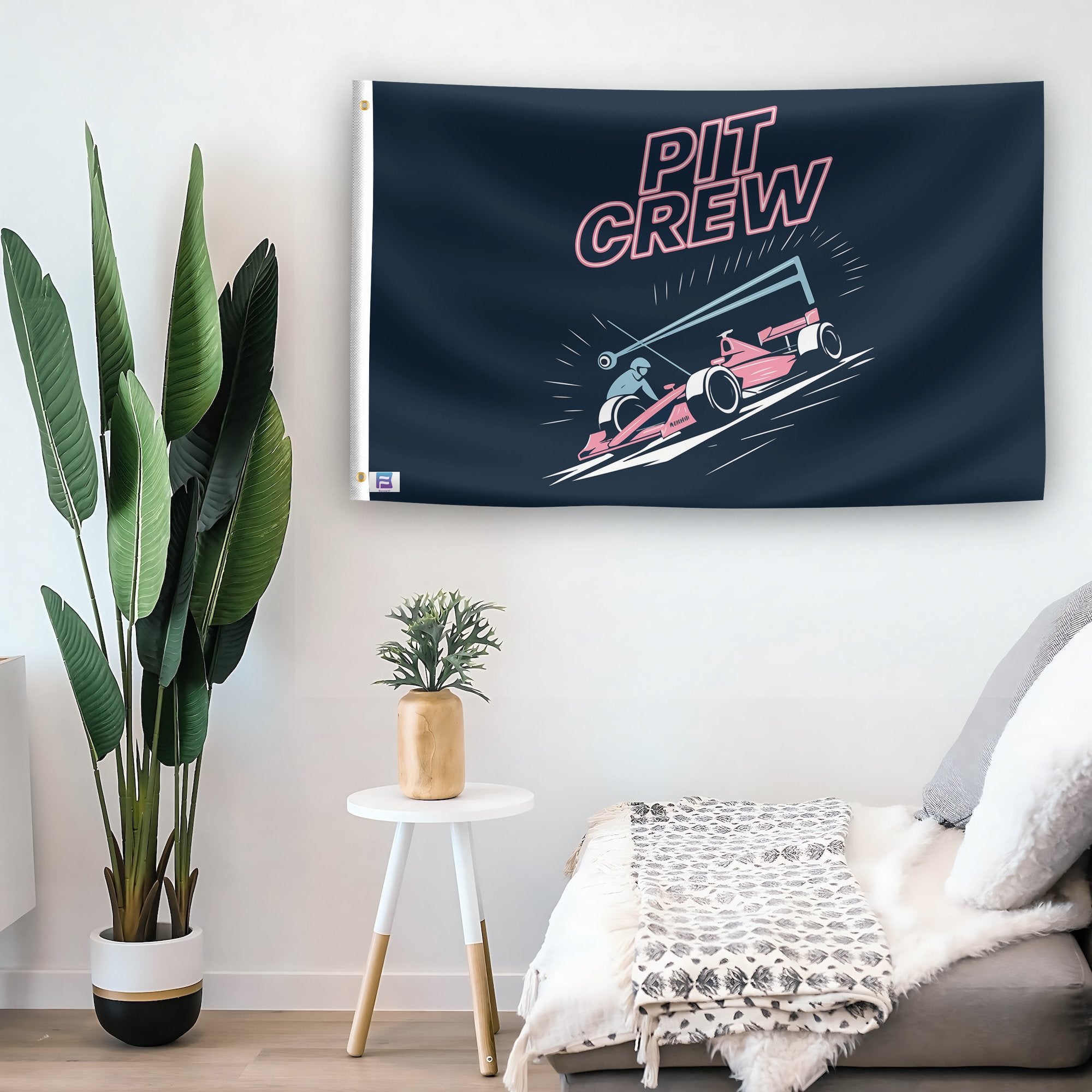 In a home setting, a flag with the saying "PIT Crew" is mounted on a white wall by a side table.