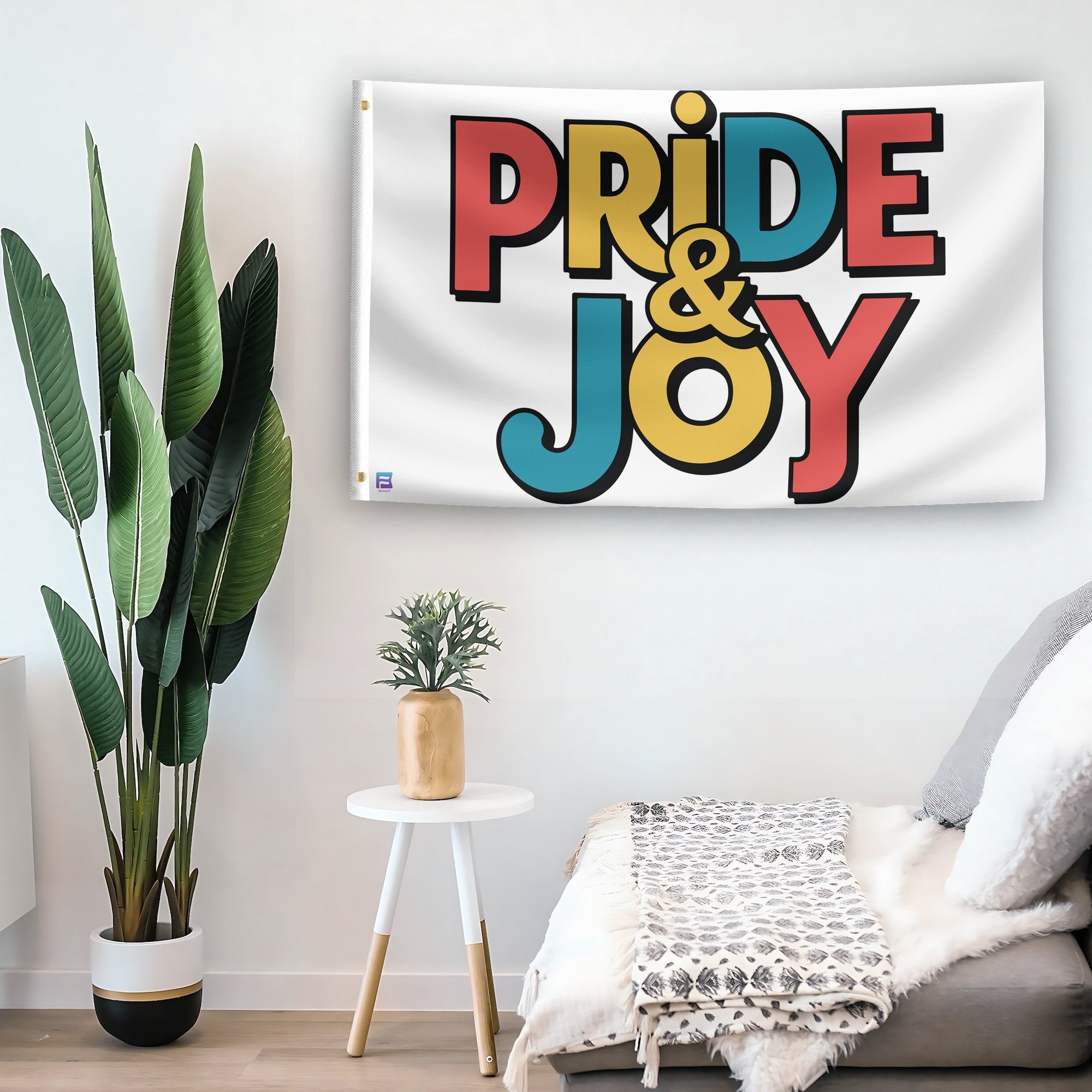 In a home setting, a flag with the saying "Pride & Joy" is mounted on a white wall by a side table.