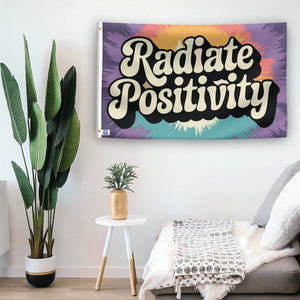 In a home setting, a flag with the saying "Radiate Positivity" is mounted on a white wall by a side table.