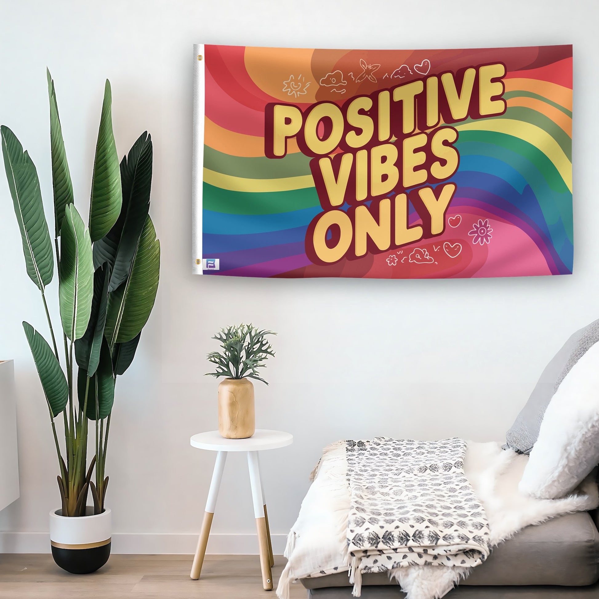 In a home setting, a flag with the saying "Positive Vibes Only" is mounted on a white wall by a side table.