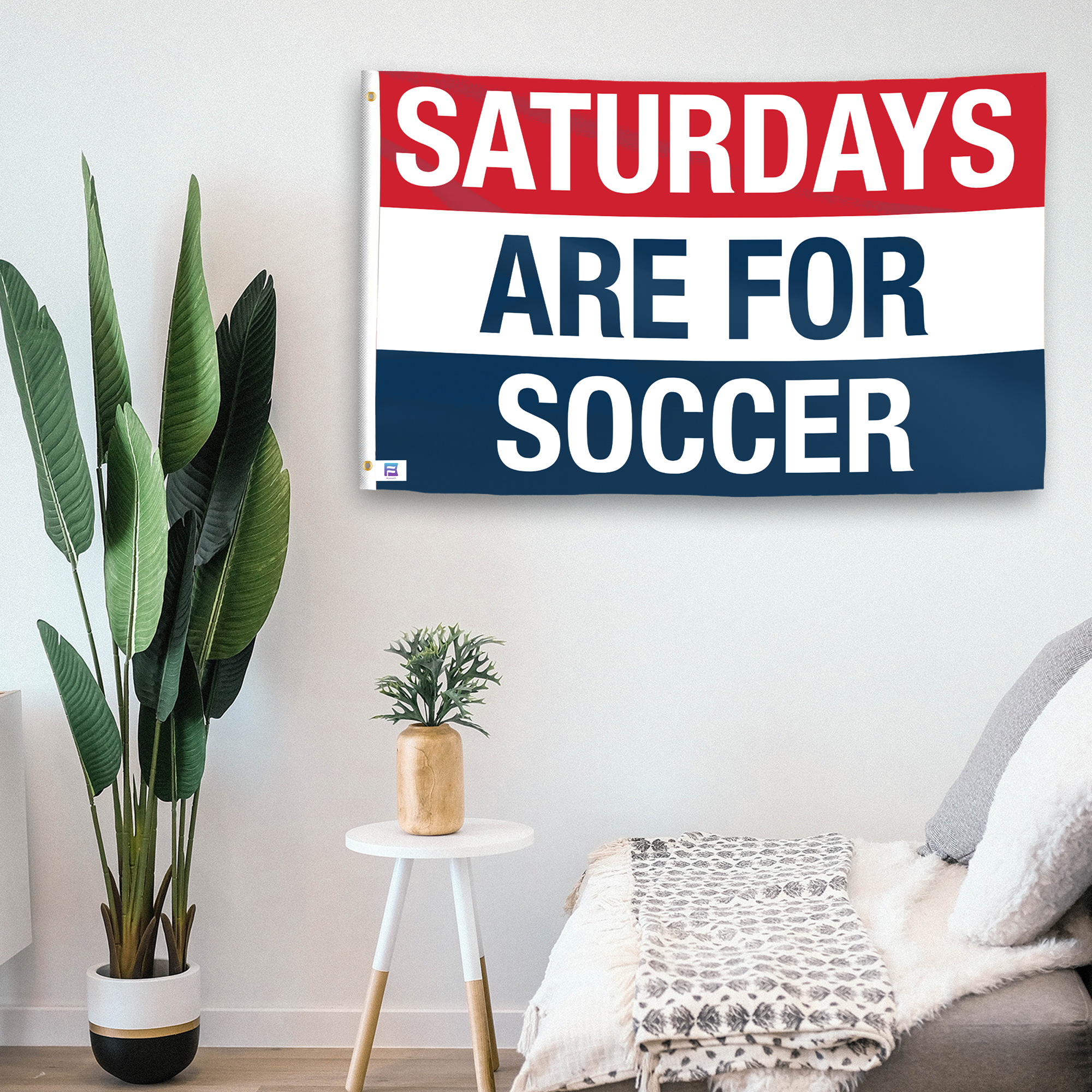 In a home setting, a flag with the saying "https://www.dropbox.com/scl/fi/gtekcy7picz4257v74zzc/saturdays-are-for-soccer_room.png?rlkey=zr5wqutdxavpojo1j5rybv42b&raw=1" is mounted on a white wall by a side table.