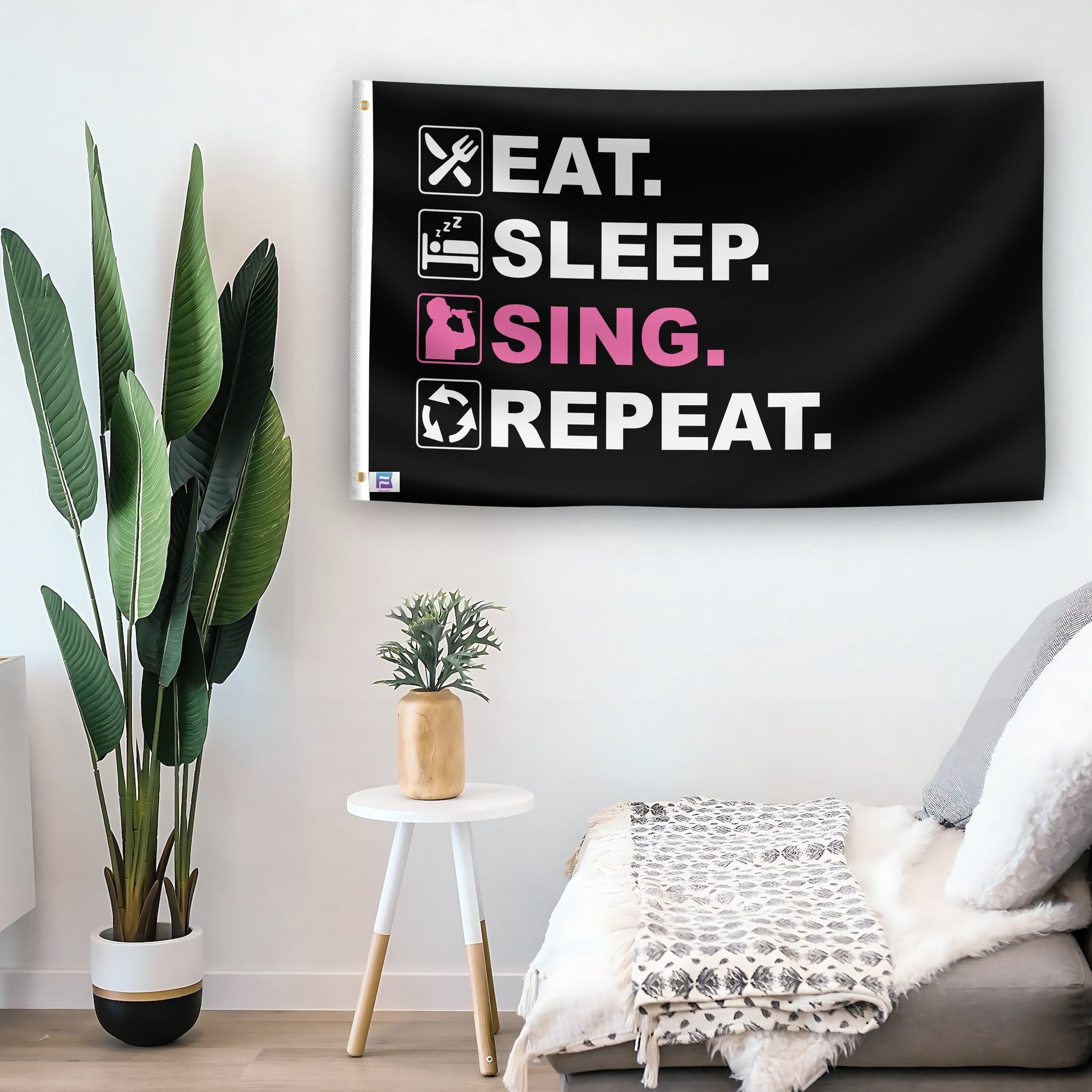 In a home setting, a flag with the saying "Eat Sleep Sing Repeat" is mounted on a white wall by a side table.