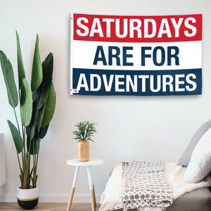 In a home setting, a flag with the saying "https://www.dropbox.com/scl/fi/a3uvnzeoqqspy2xpx88l1/saturdays-are-for-adventures_room.png?rlkey=dztbwnazw8t8gsw8o72quqydb&raw=1" is mounted on a white wall by a side table.