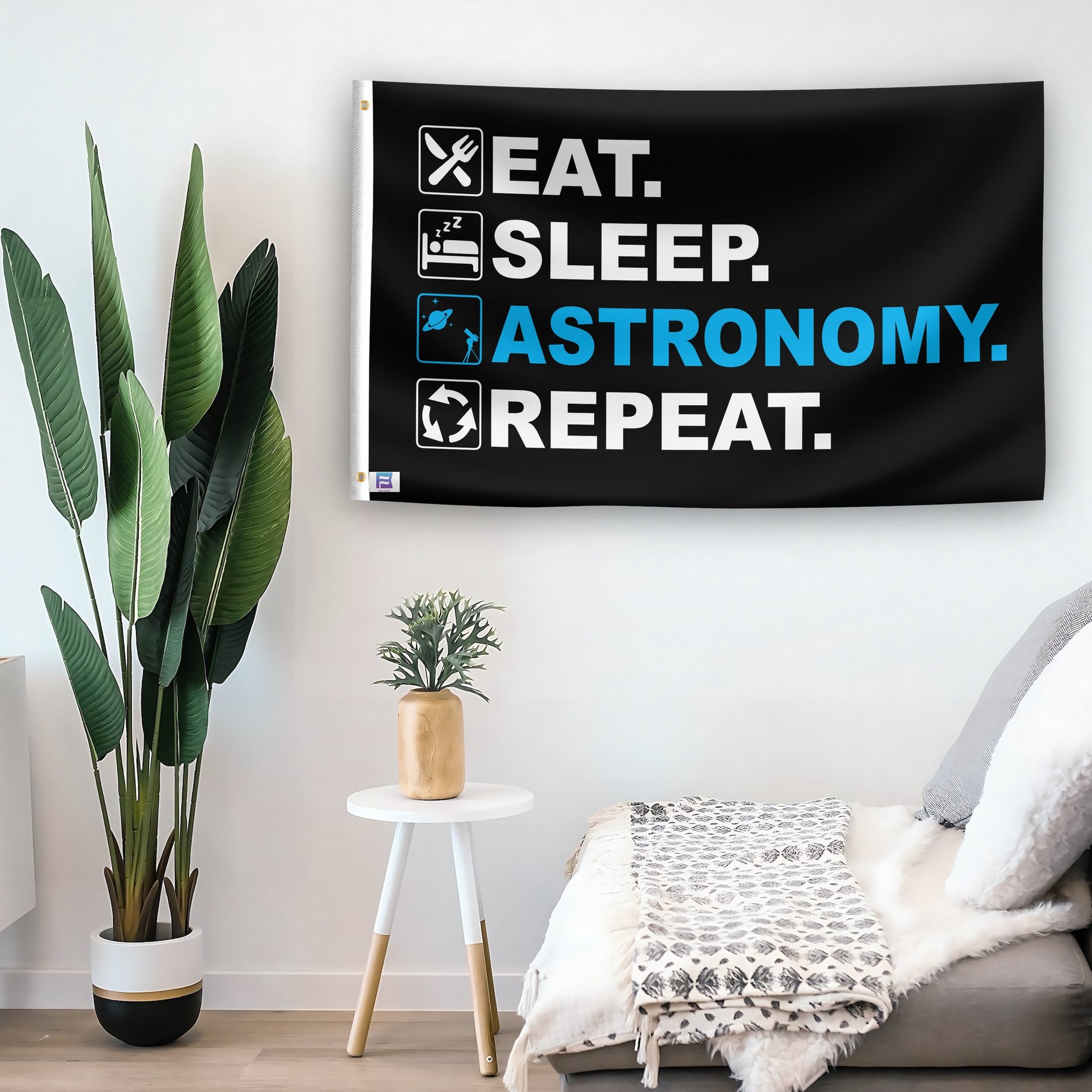 In a home setting, a flag with the saying "Eat Sleep Astronomy Repeat" is mounted on a white wall by a side table.