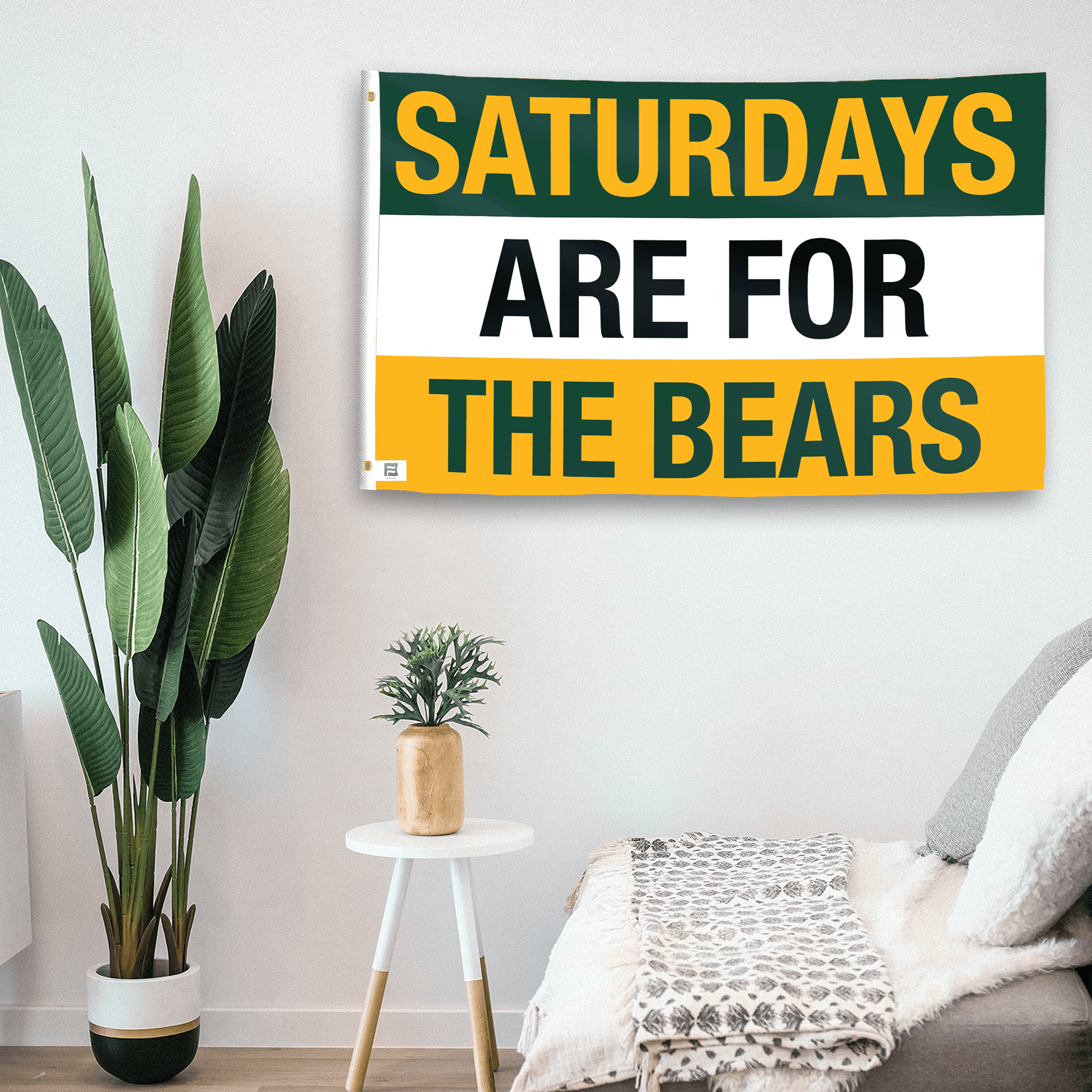 In a home setting, a flag with the saying "Saturdays Are for the Bears" is mounted on a white wall by a side table.