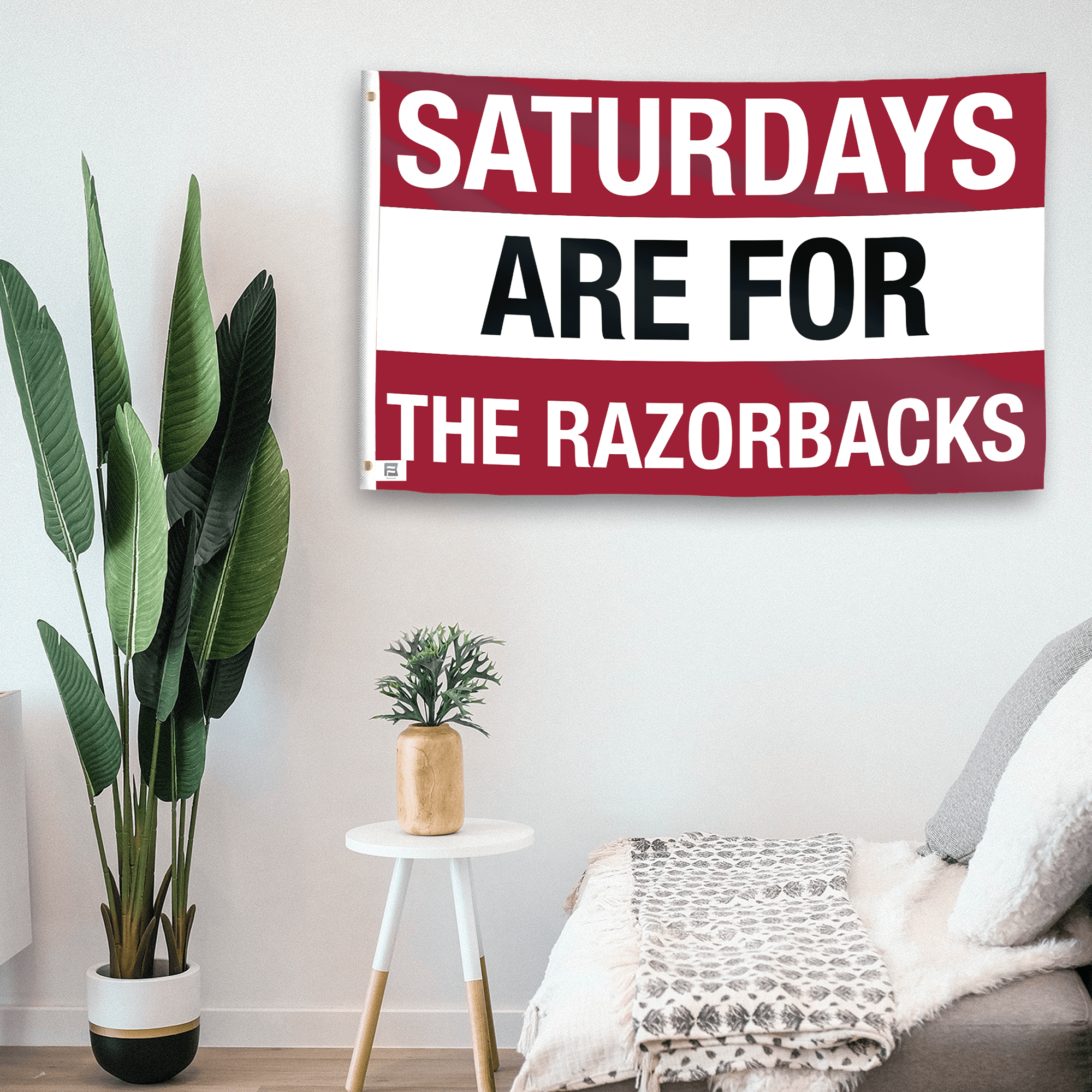 In a home setting, a flag with the saying "Saturdays Are for the Razorbacks" is mounted on a white wall by a side table.