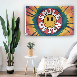 In a home setting, a flag with the saying "Smile Often" is mounted on a white wall by a side table.