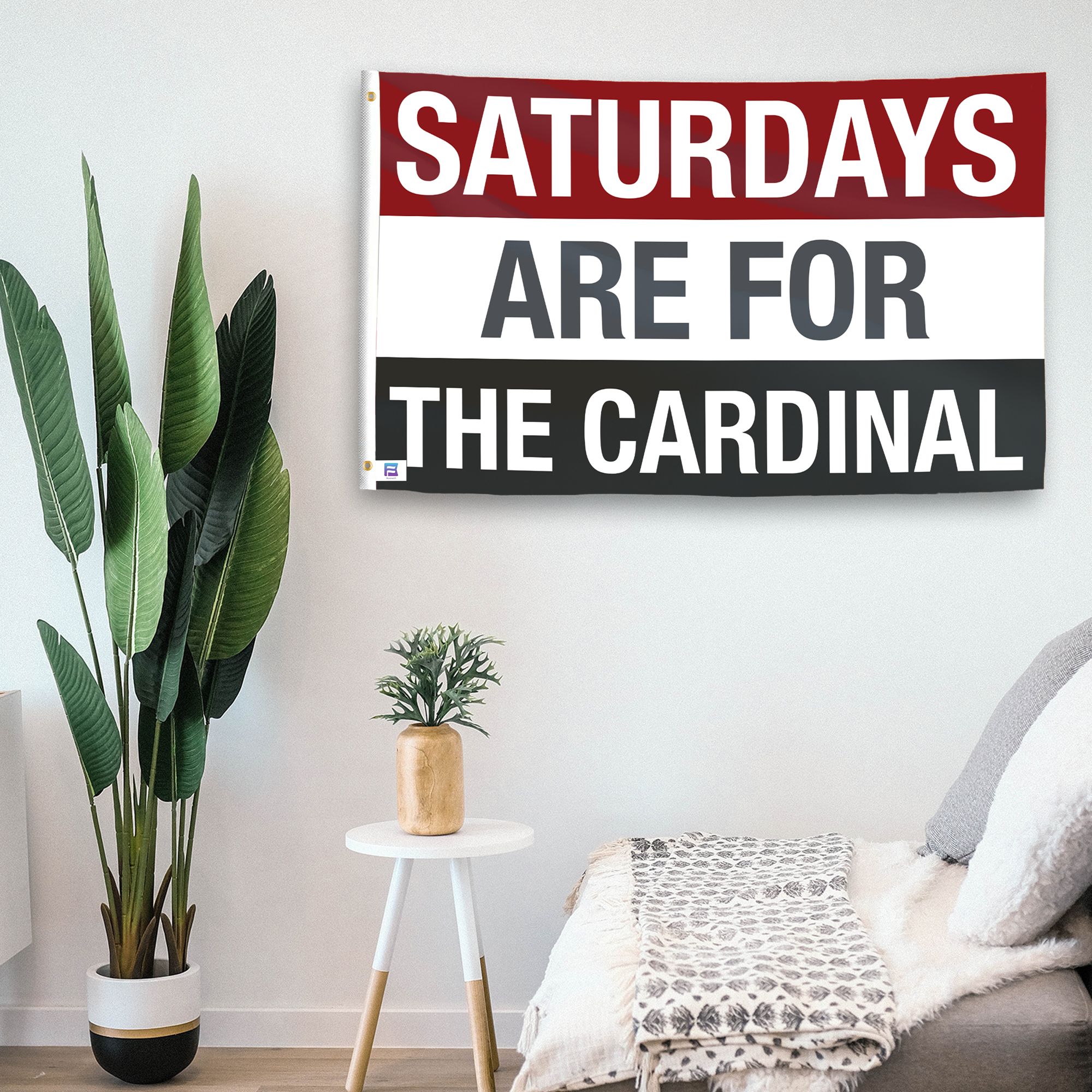 In a home setting, a flag with the saying "Saturdays Are for the Cardinal" is mounted on a white wall by a side table.