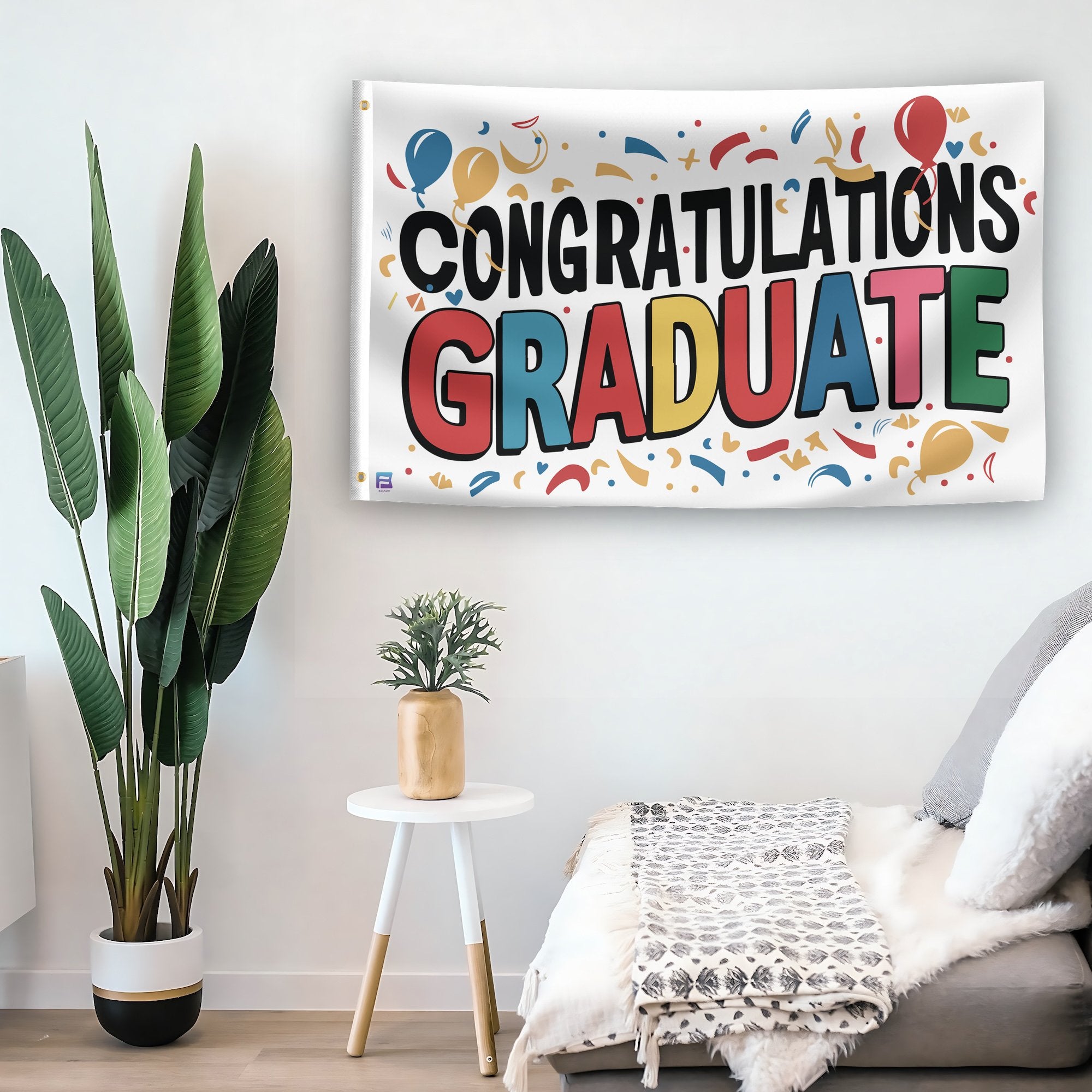 In a home setting, a flag with the saying "Congratulations Graduate" is mounted on a white wall by a side table.