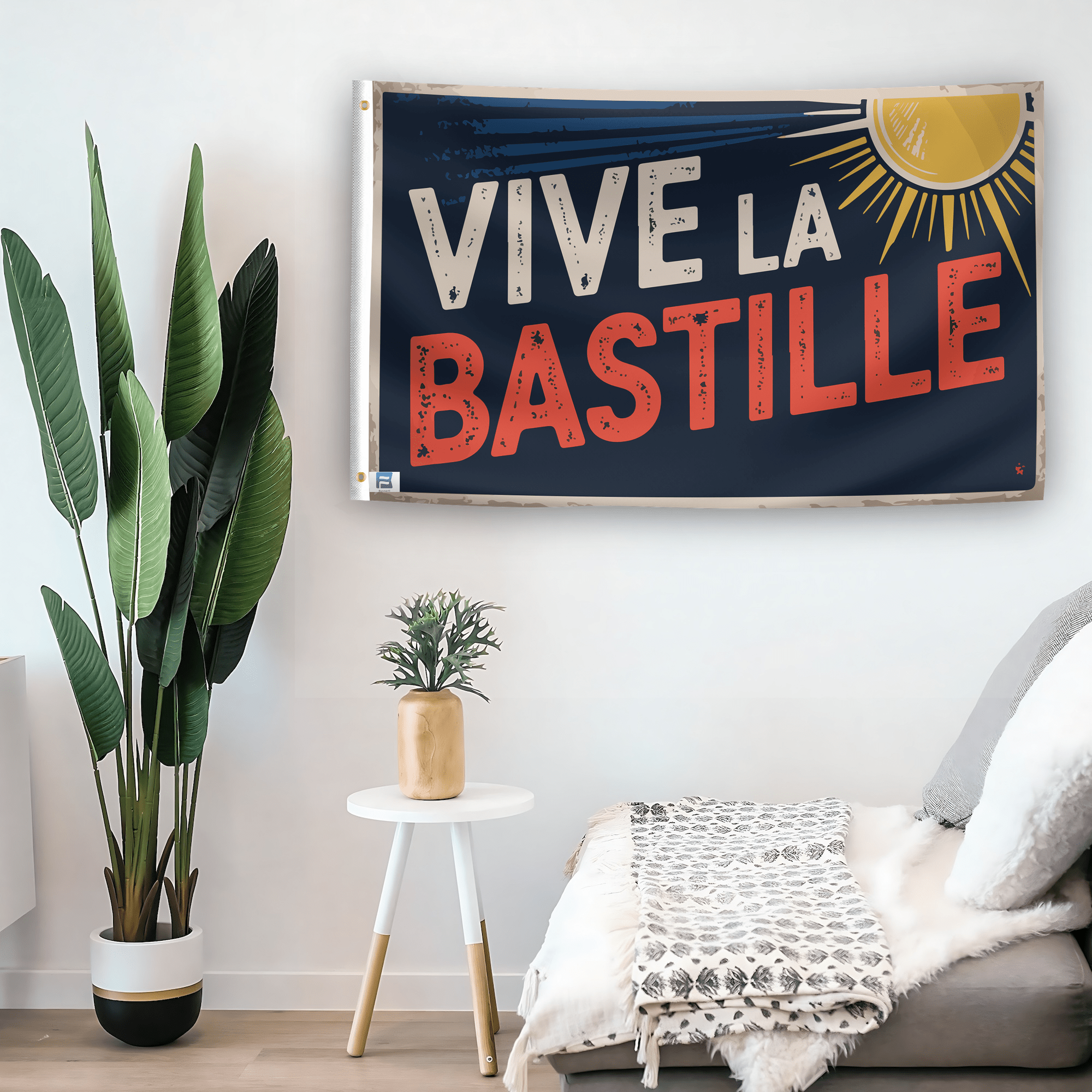 In a home setting, a flag with the saying "Vive La Bastille" is mounted on a white wall by a side table.