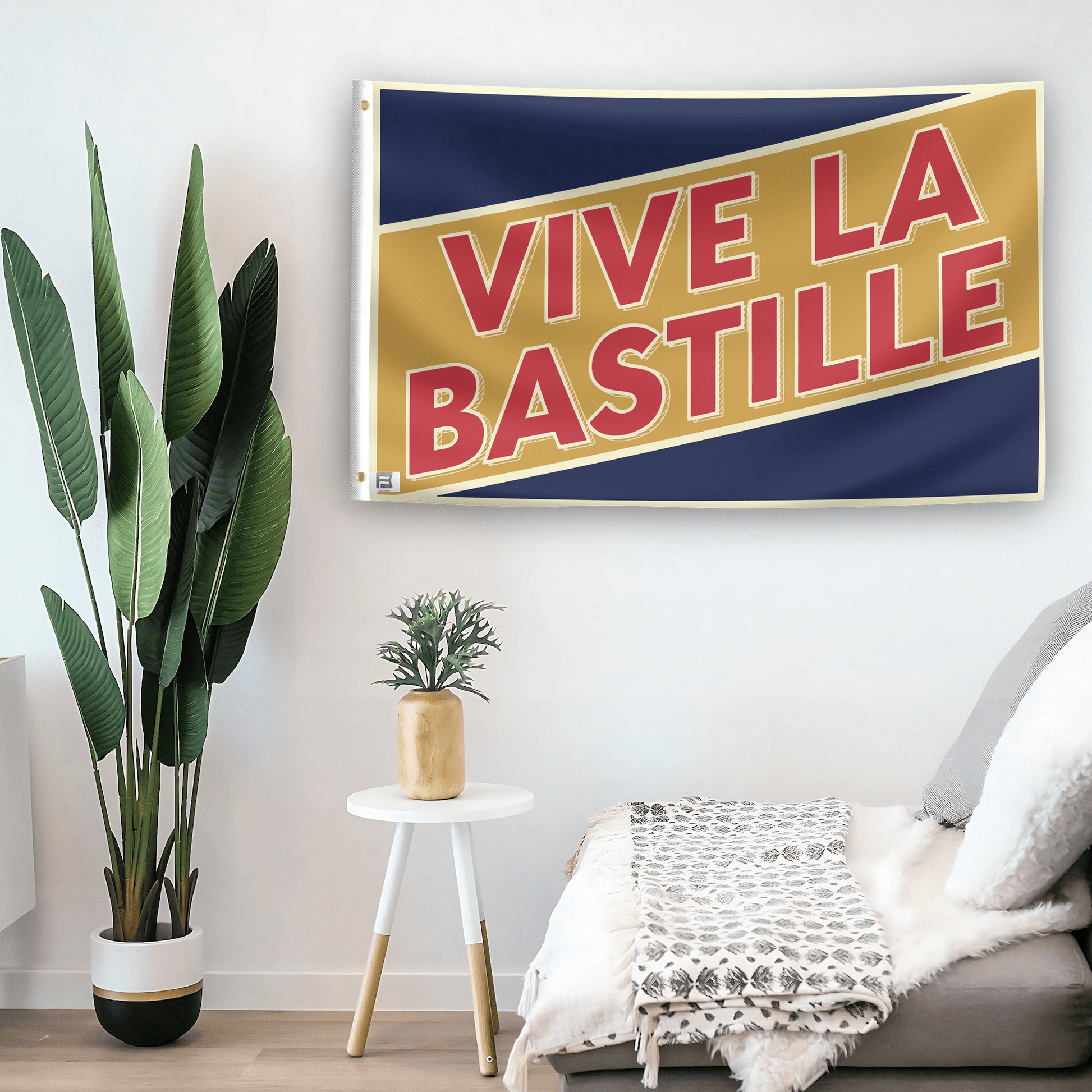 In a home setting, a flag with the saying "Vive La Bastille Holiday" is mounted on a white wall by a side table.