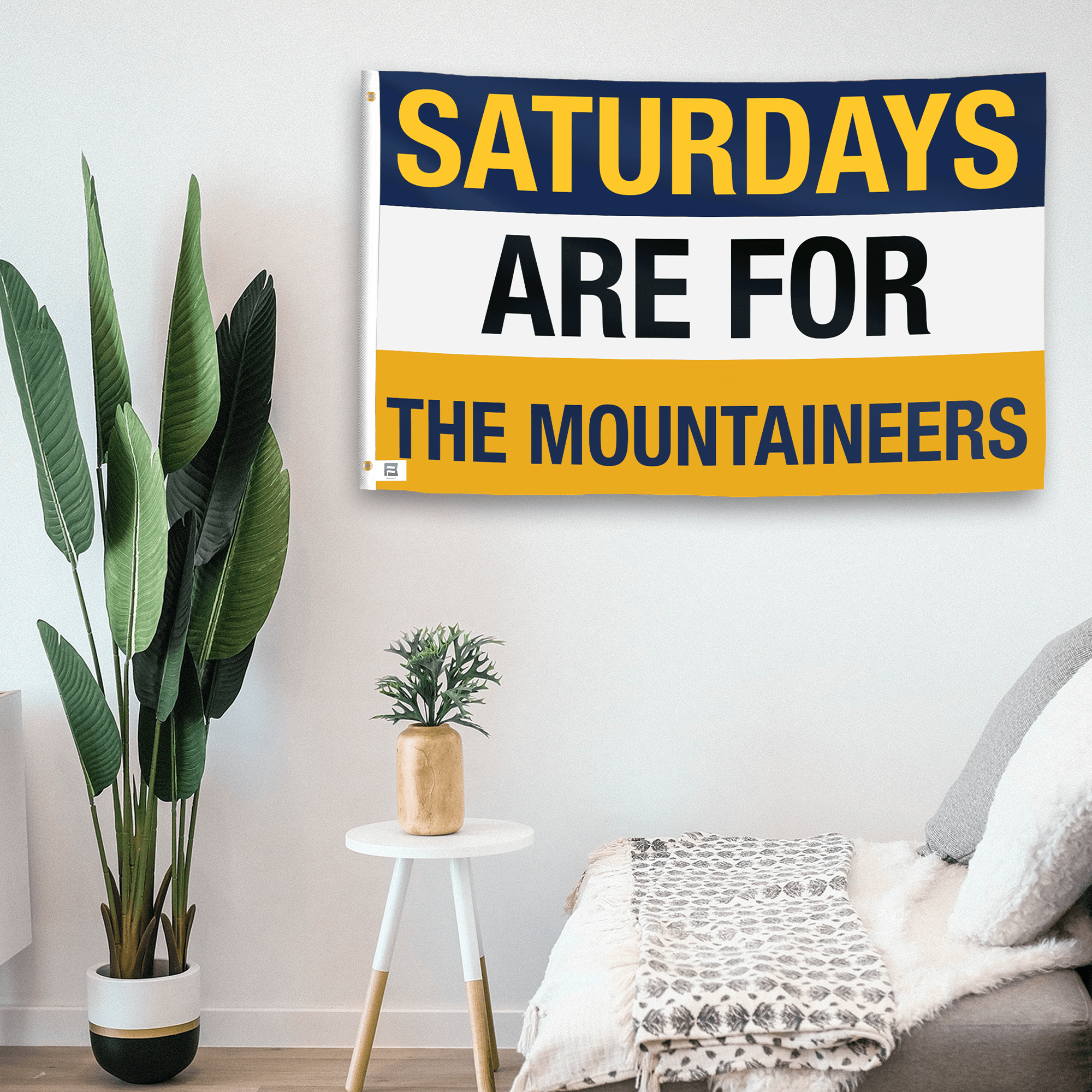 In a home setting, a flag with the saying "Saturdays Are for the Mountaineers" is mounted on a white wall by a side table.