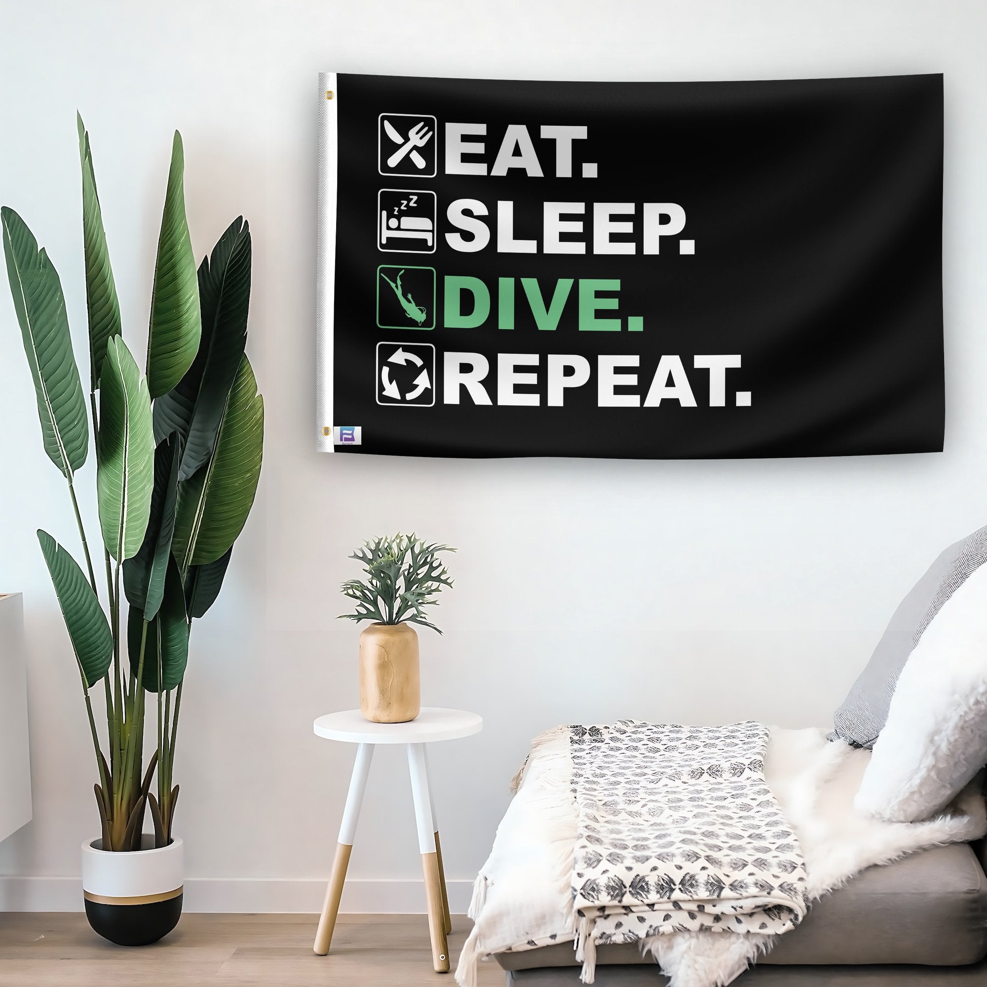 In a home setting, a flag with the saying "Eat Sleep Dive Repeat" is mounted on a white wall by a side table.