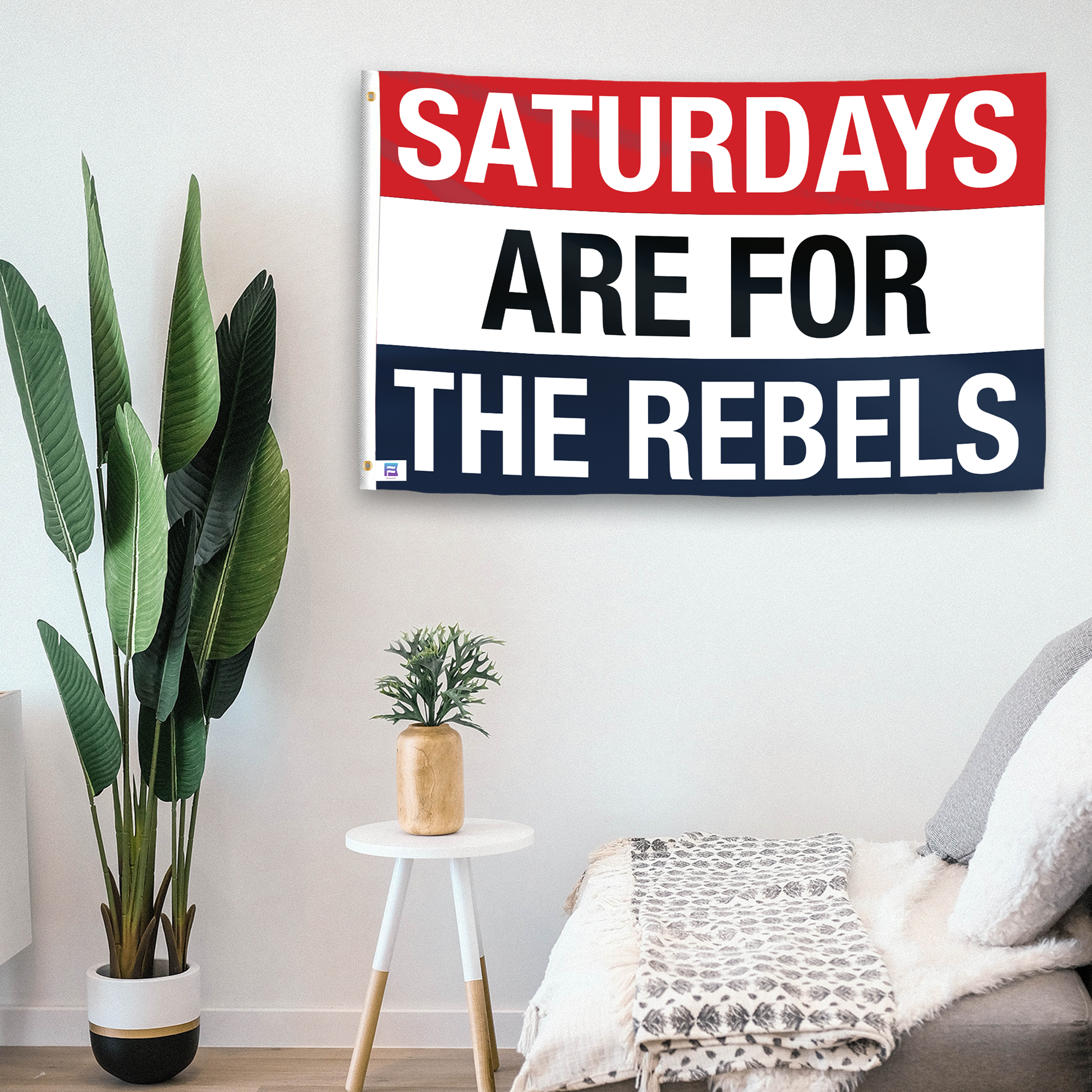 In a home setting, a flag with the saying "Saturdays Are for the Rebels" is mounted on a white wall by a side table.