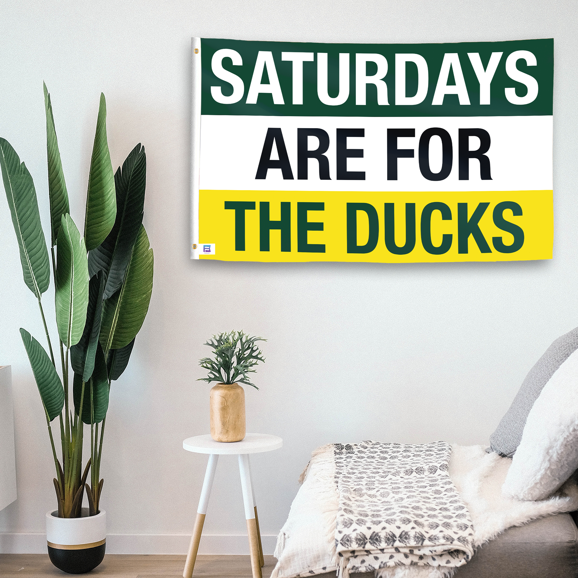 In a home setting, a flag with the saying "Saturdays Are for the Ducks" is mounted on a white wall by a side table.