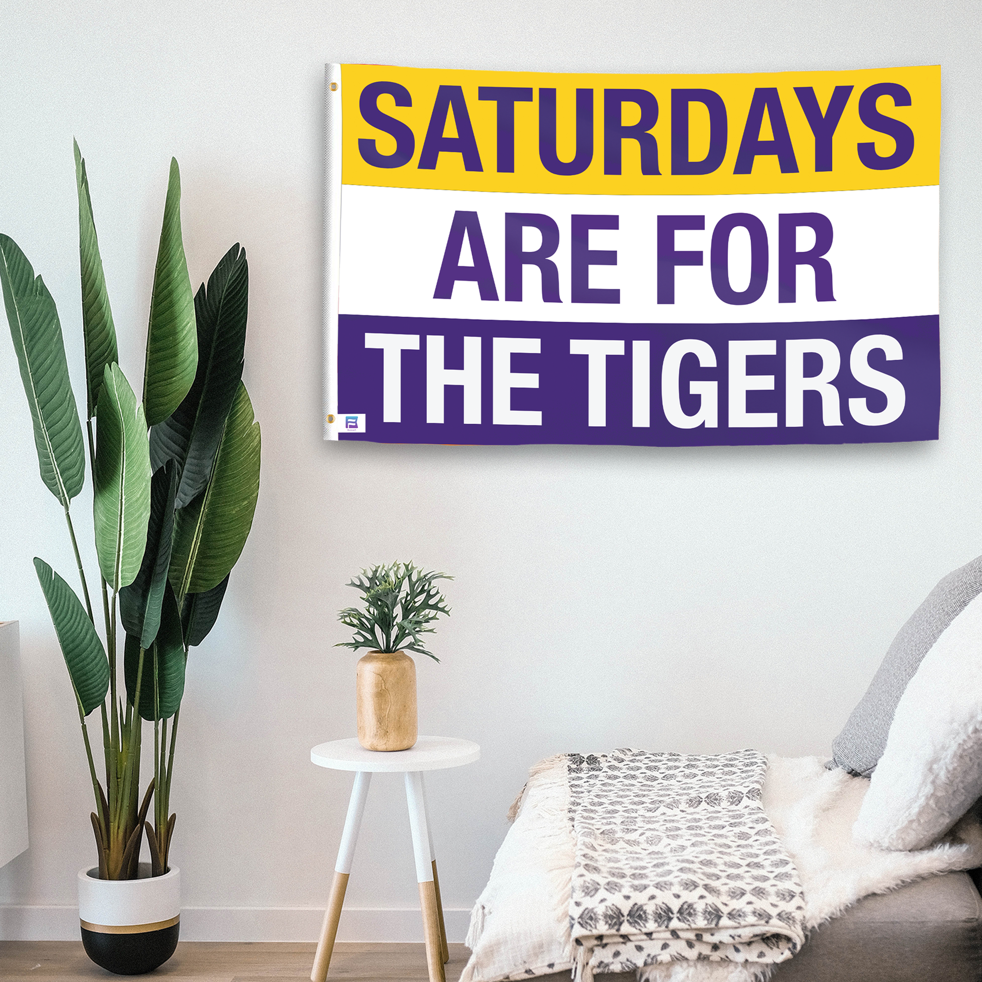 In a home setting, a flag with the saying "Saturdays Are for the Tigers LSU" is mounted on a white wall by a side table.