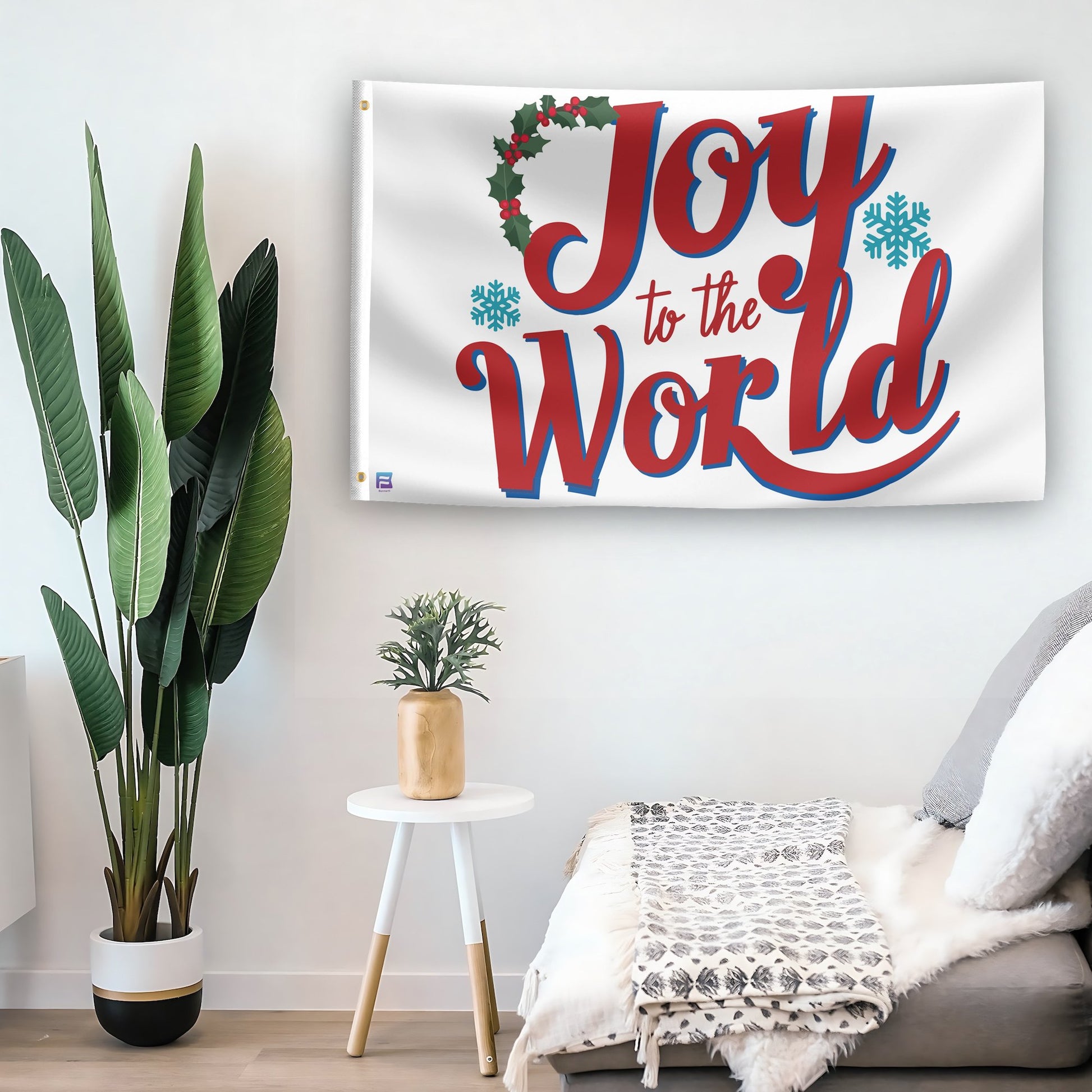 In a home setting, a flag with the saying "Joy To The World Christmas" is mounted on a white wall by a side table.