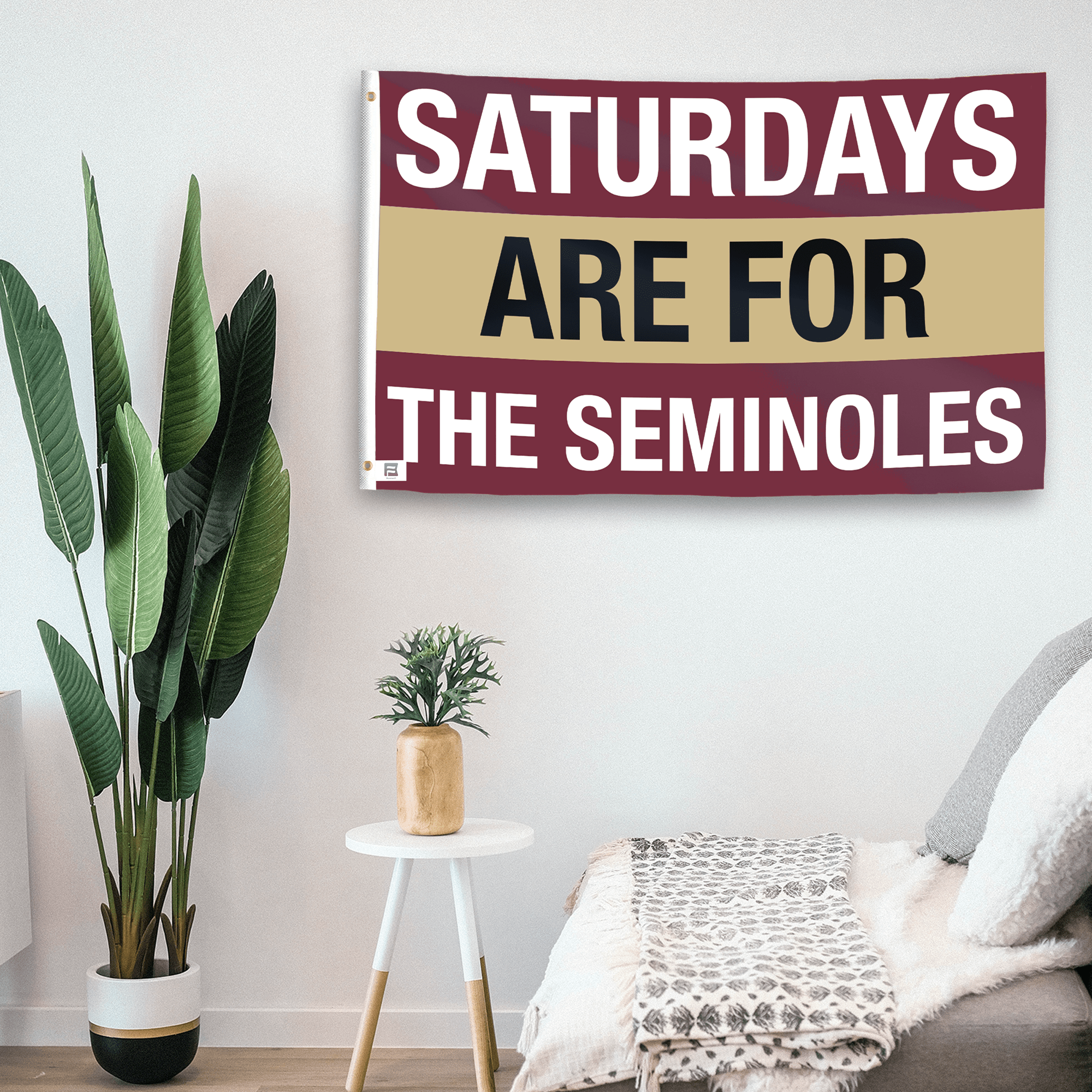 In a home setting, a flag with the saying "Saturdays Are for the Seminoles" is mounted on a white wall by a side table.