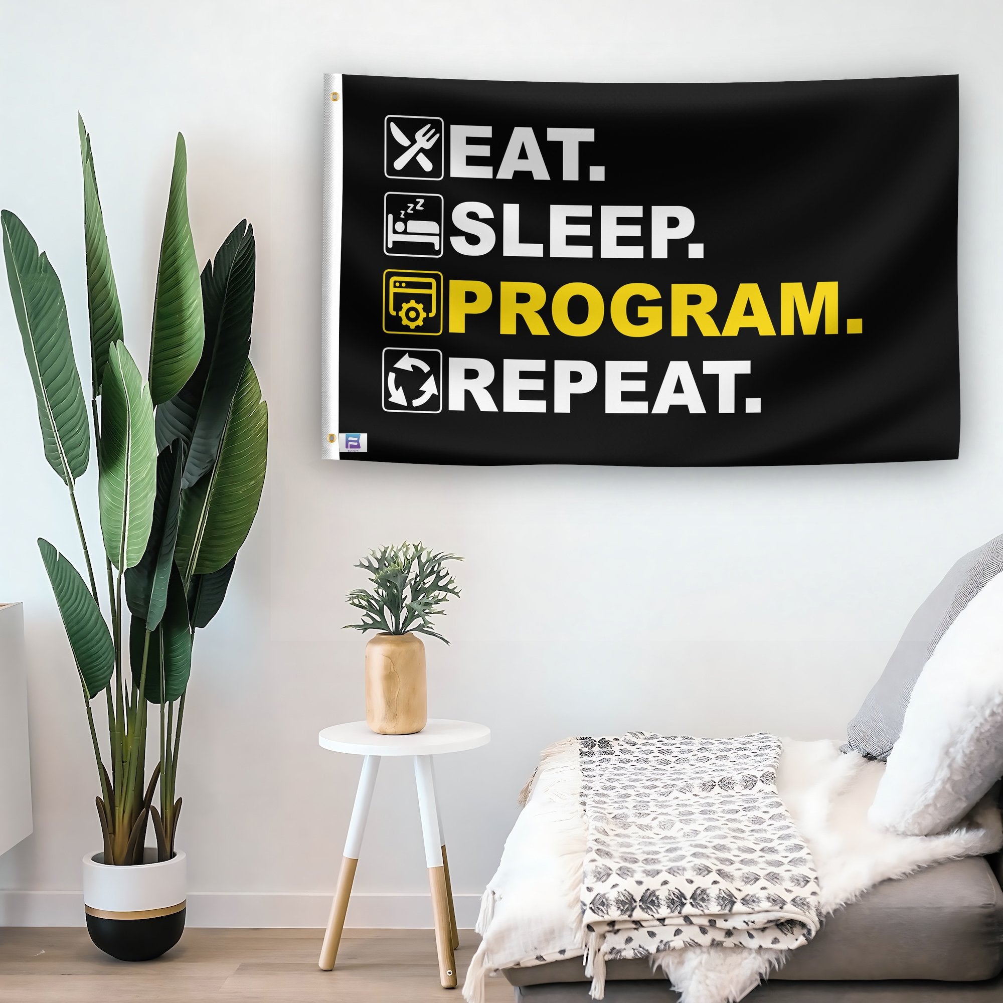 In a home setting, a flag with the saying "Eat Sleep Program Repeat" is mounted on a white wall by a side table.