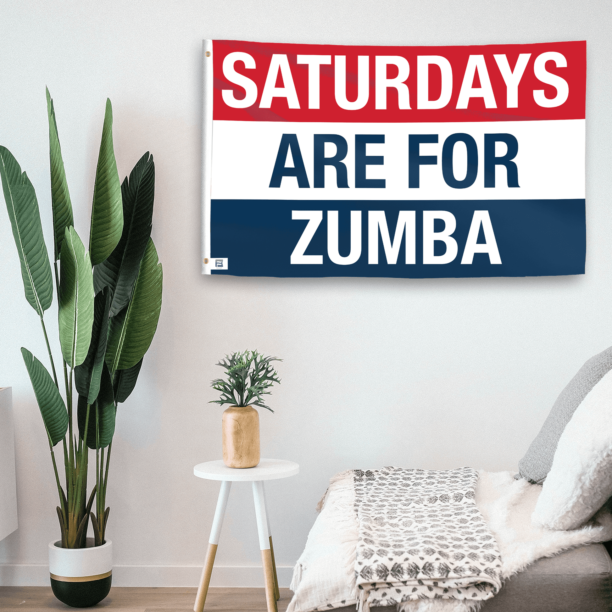 In a home setting, a flag with the saying "https://www.dropbox.com/scl/fi/fk9niv3qymr6jqh4zqn7z/saturdays-are-for-zumba_room.png?rlkey=fb258xzsmrslfn1ytq3tubtms&raw=1" is mounted on a white wall by a side table.