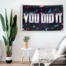 Load image into Gallery viewer, In a home setting, a flag with the saying &quot;You Did It&quot; is mounted on a white wall by a side table.
