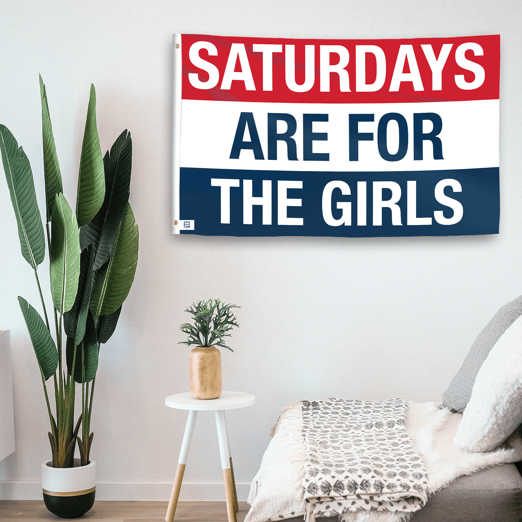 In a home setting, a flag with the saying "https://www.dropbox.com/scl/fi/qklk3qzoxlzp4mh45a74r/saturdays-are-for-the-girls_room.png?rlkey=9hinrlutm3iz0naqubtzgganq&raw=1" is mounted on a white wall by a side table.