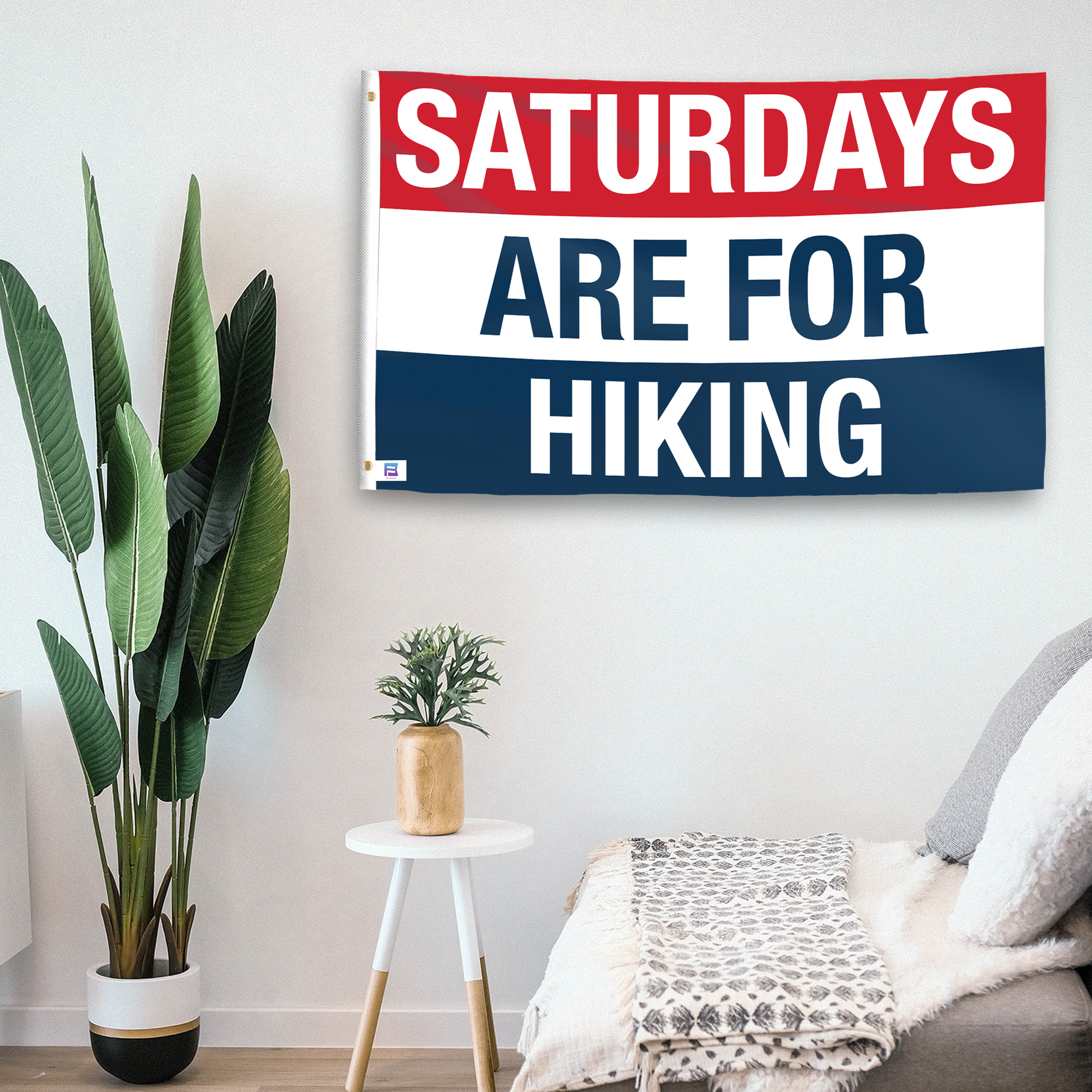 In a home setting, a flag with the saying "https://www.dropbox.com/scl/fi/vi52n7qsz5wlk585ebx7w/saturdays-are-for-hiking_room.png?rlkey=sv6kzp46u4jmyenm02x5qk3vt&raw=1" is mounted on a white wall by a side table.