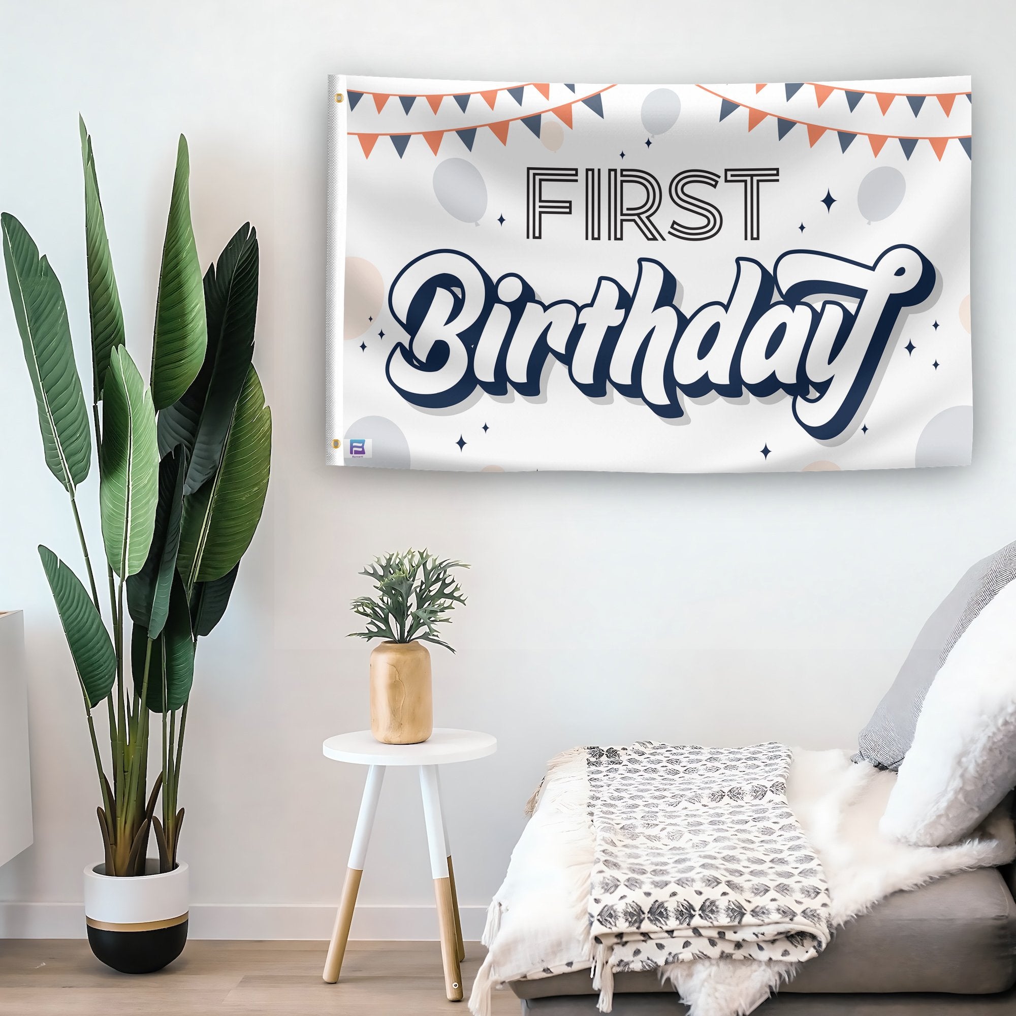 In a home setting, a flag with the saying "First Birthday" is mounted on a white wall by a side table.