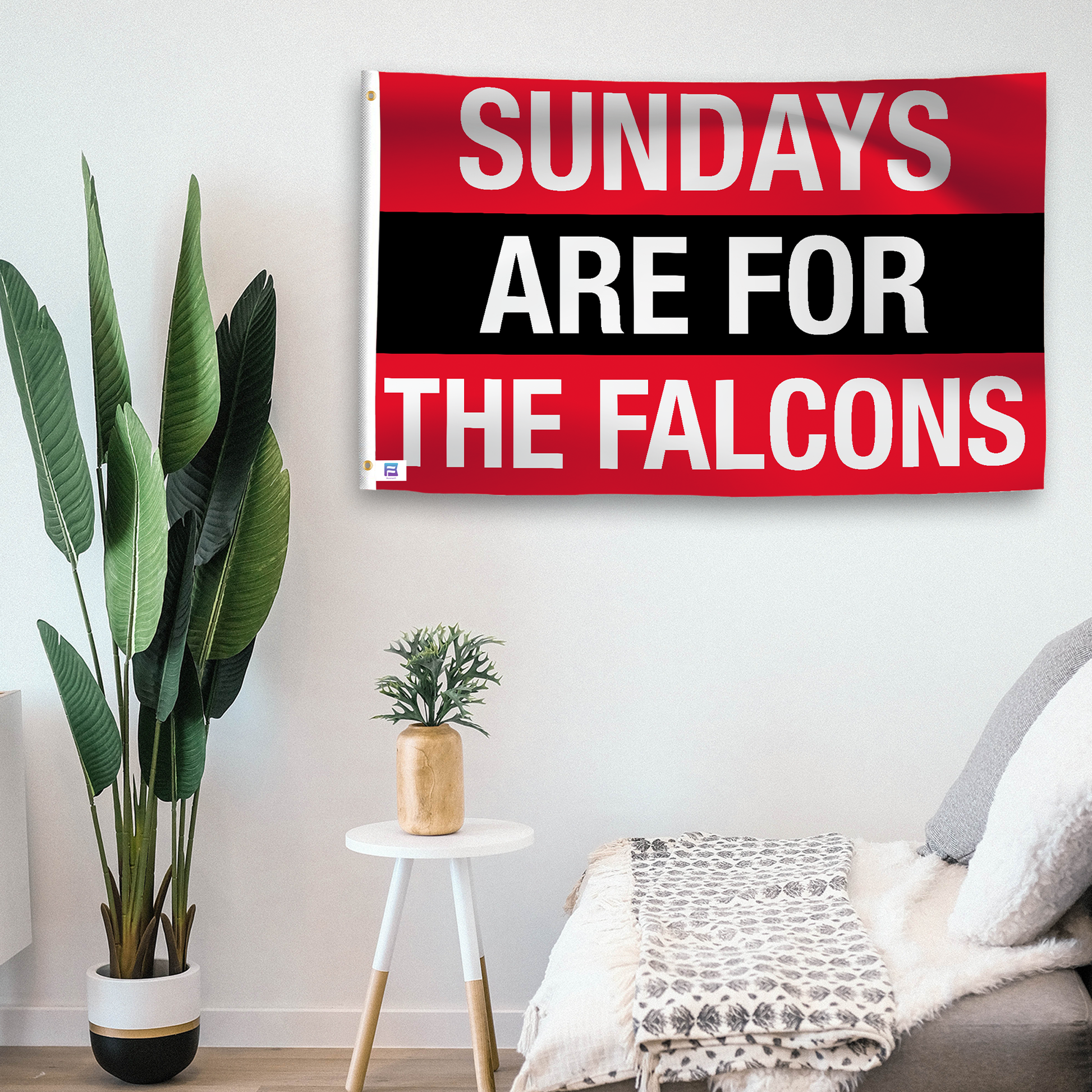 In a home setting, a flag with the saying "https://www.dropbox.com/scl/fi/luf89g3bss9p5z6za88b9/sundays-are-for-the-falcons_room.png?rlkey=e04e9oou8uzytipb7mgzgdjb1&raw=1" is mounted on a white wall by a side table.