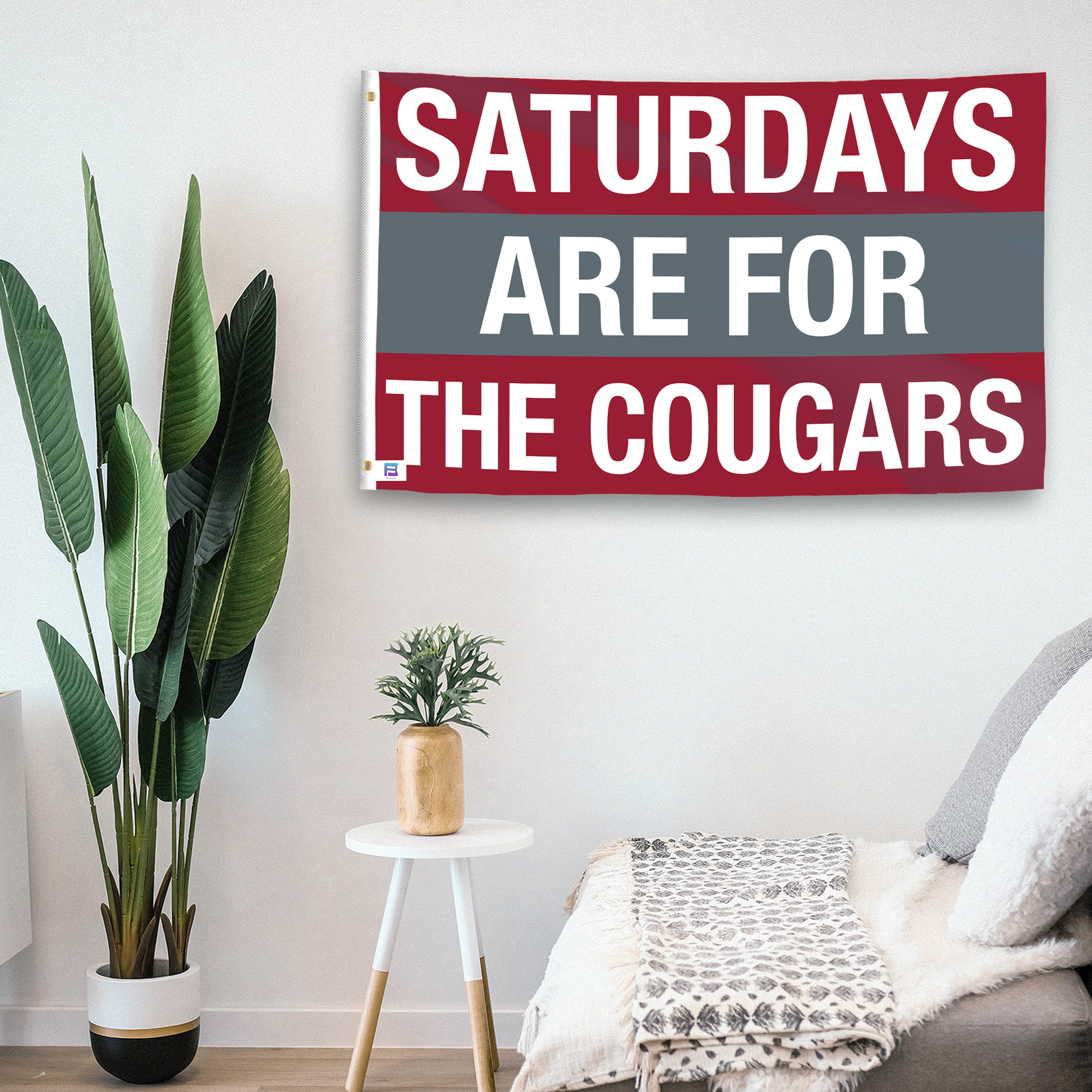 In a home setting, a flag with the saying "Saturdays Are for the Cougars Washington State" is mounted on a white wall by a side table.