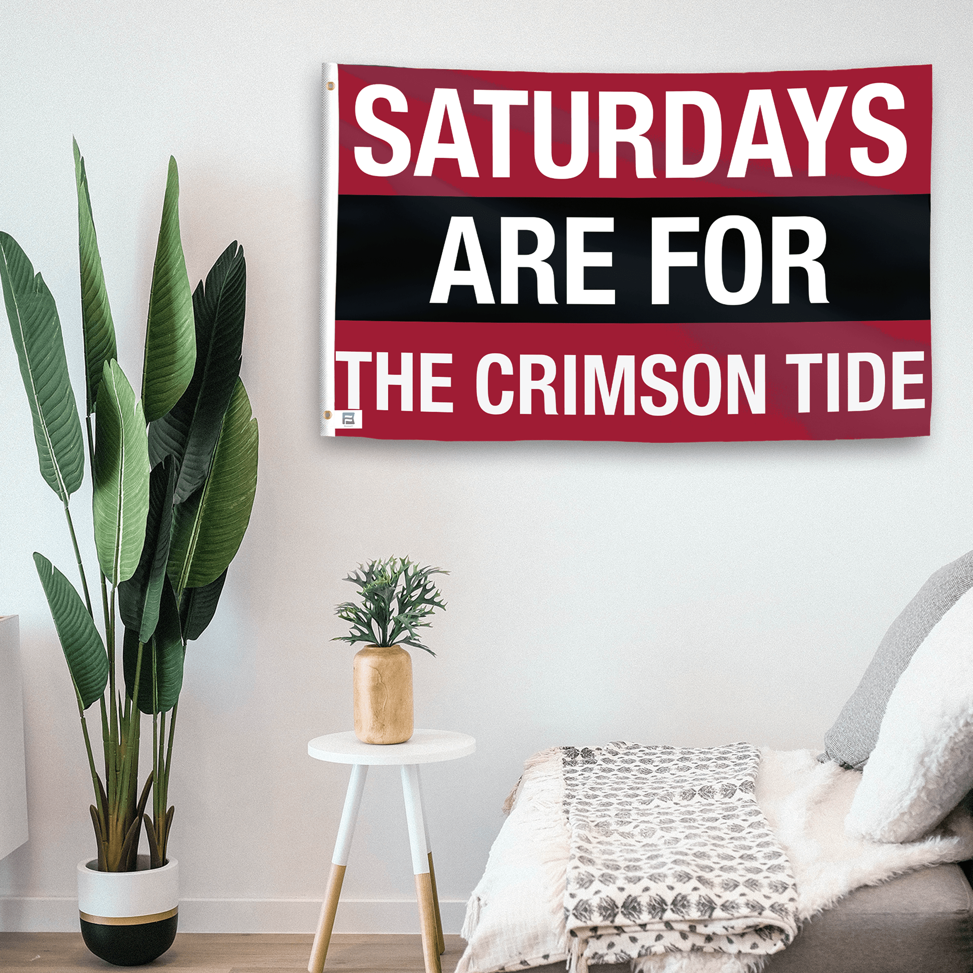 In a home setting, a flag with the saying "Saturdays Are for the Crimson Tide" is mounted on a white wall by a side table.