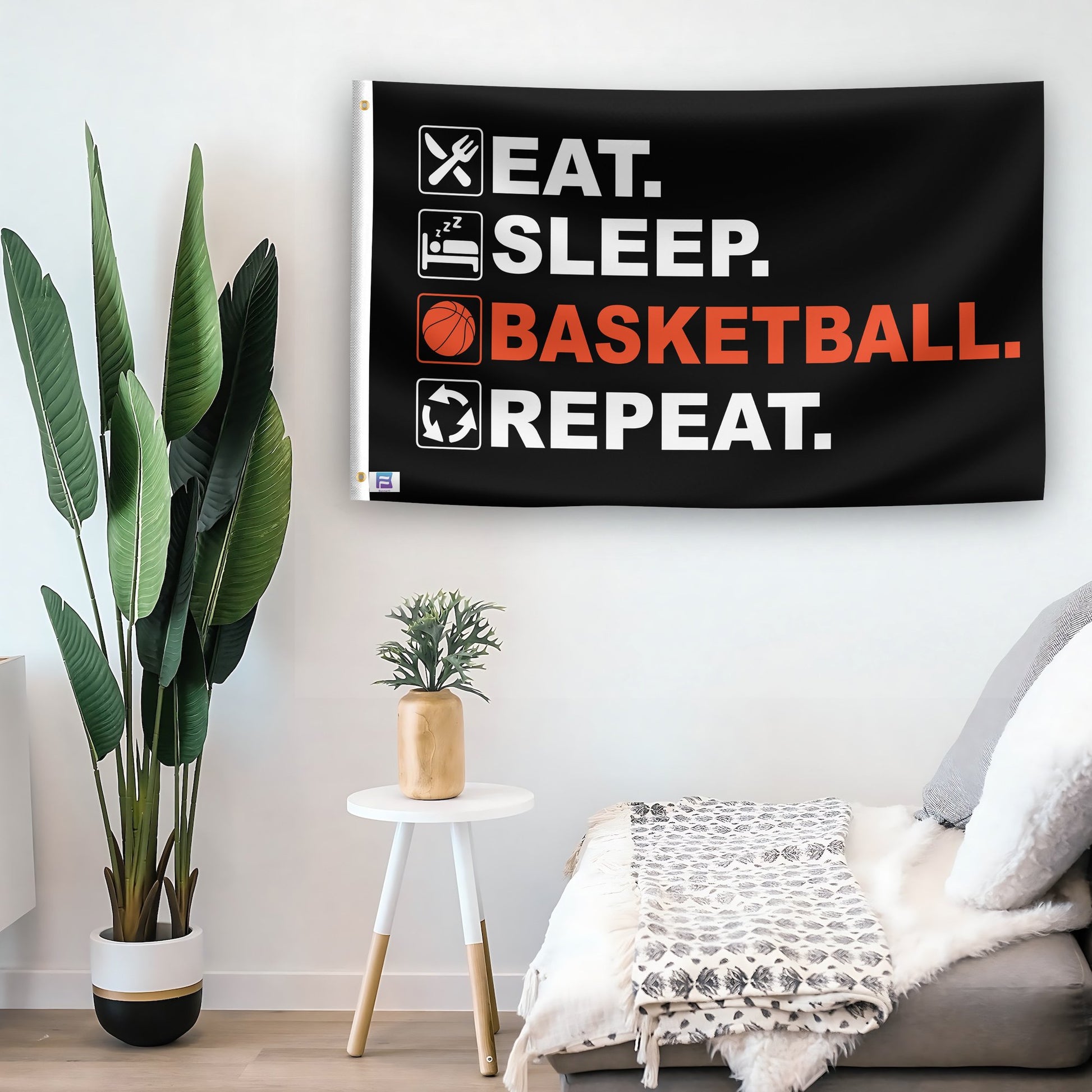 In a home setting, a flag with the saying "Eat Sleep Basketball Repeat" is mounted on a white wall by a side table.