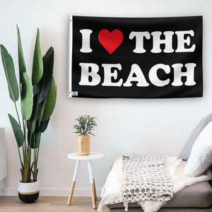 In a home setting, a flag with the saying "I Love The Beach" is mounted on a white wall by a side table.