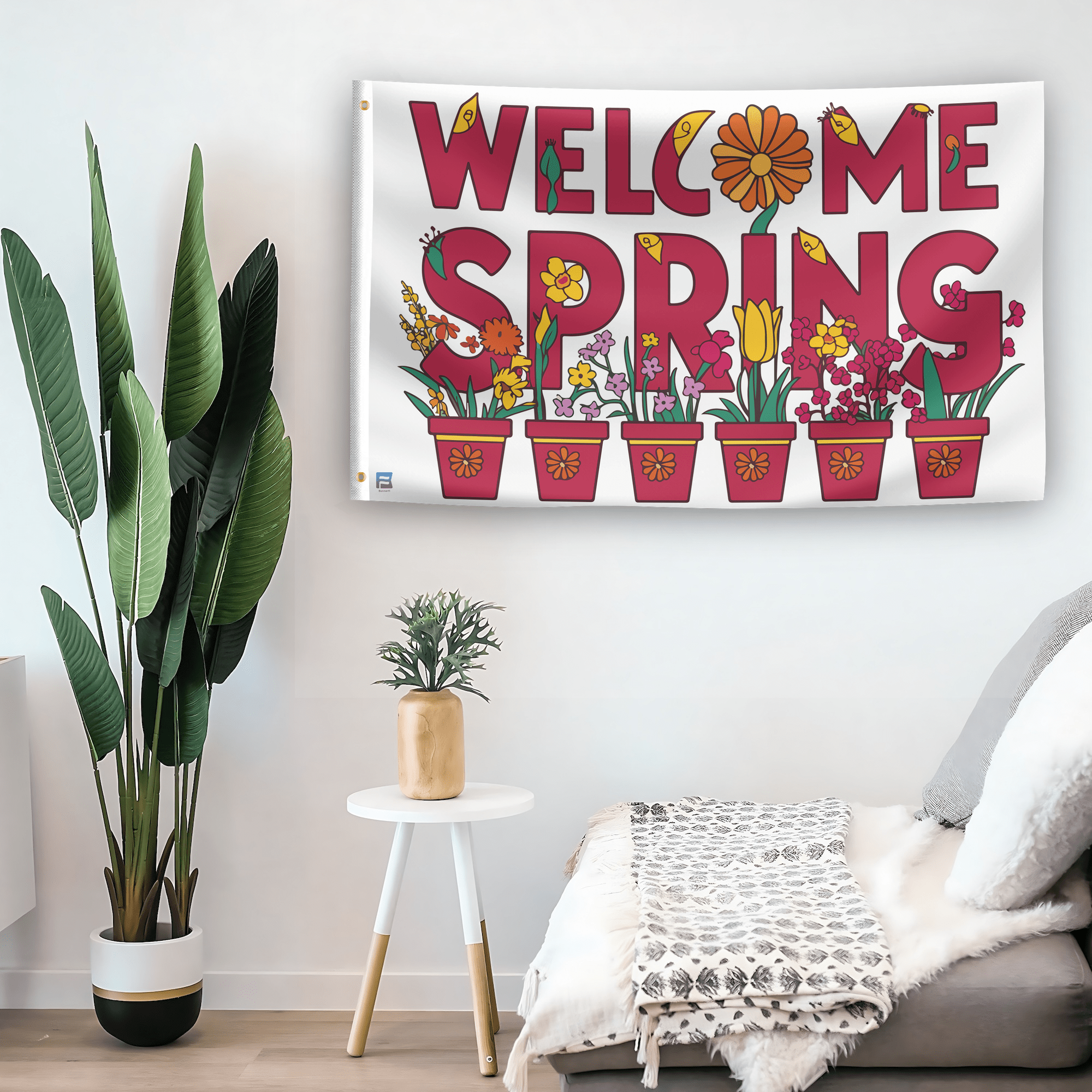 In a home setting, a flag with the saying "Welcome Spring Floral" is mounted on a white wall by a side table.