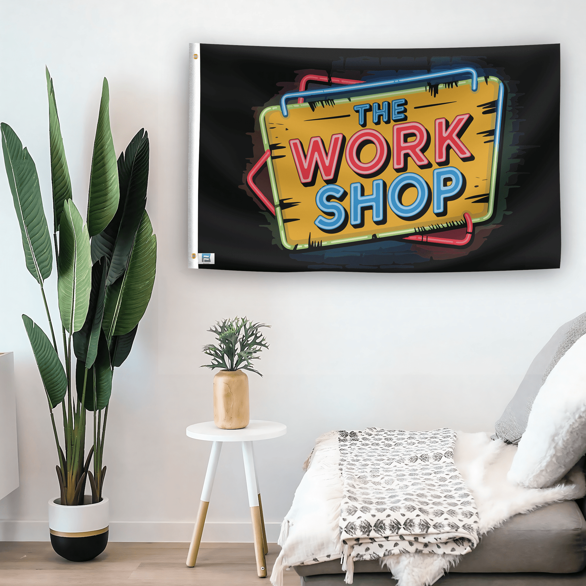 In a home setting, a flag with the saying "The Work Shop Garage" is mounted on a white wall by a side table.