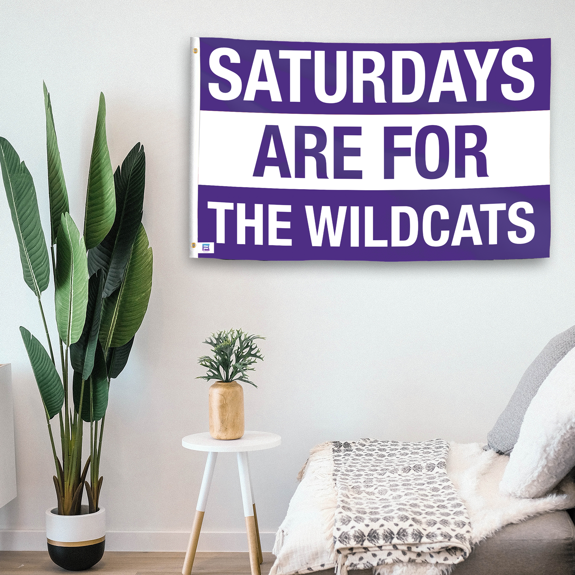 In a home setting, a flag with the saying "Saturdays Are for the Wildcats Northwestern" is mounted on a white wall by a side table.