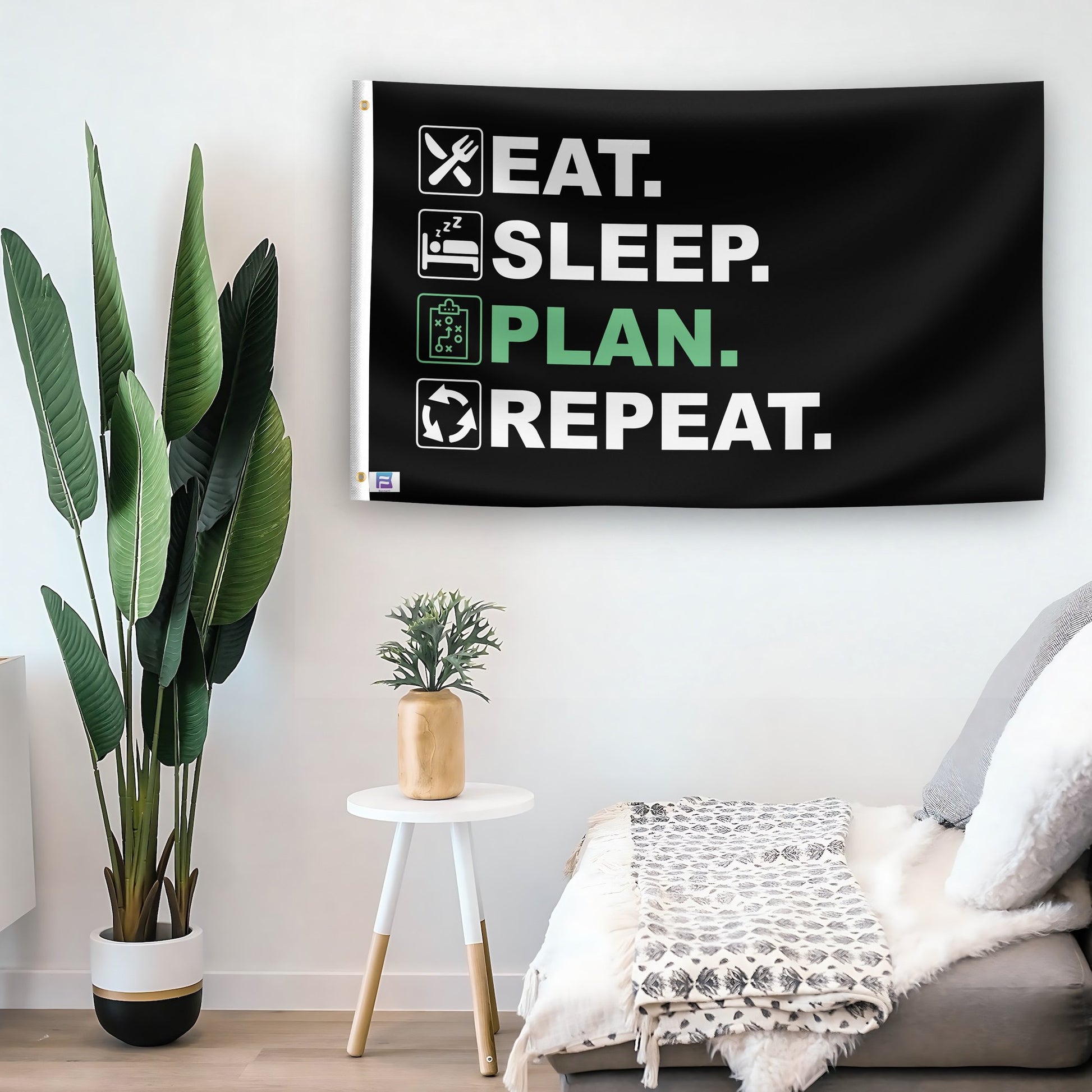 In a home setting, a flag with the saying "Eat Sleep Plan Repeat" is mounted on a white wall by a side table.