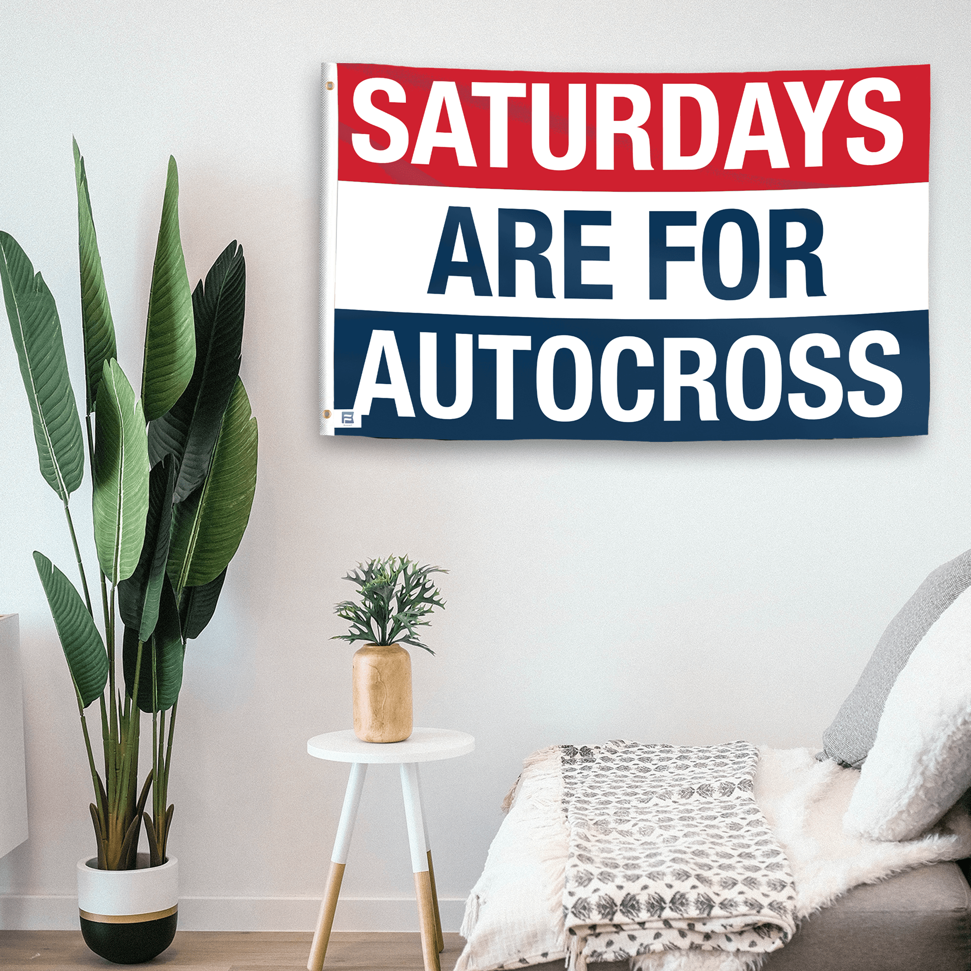 In a home setting, a flag with the saying "https://www.dropbox.com/scl/fi/7viit6k8ih62f15zw3167/saturdays-are-for-autocross_room.png?rlkey=abvm6lzegurn66o2genoapcaw&raw=1" is mounted on a white wall by a side table.