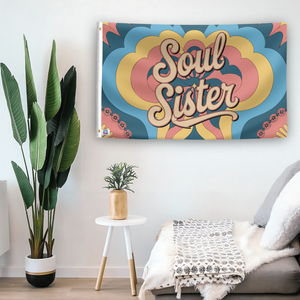 In a home setting, a flag with the saying "Soul Sister" is mounted on a white wall by a side table.