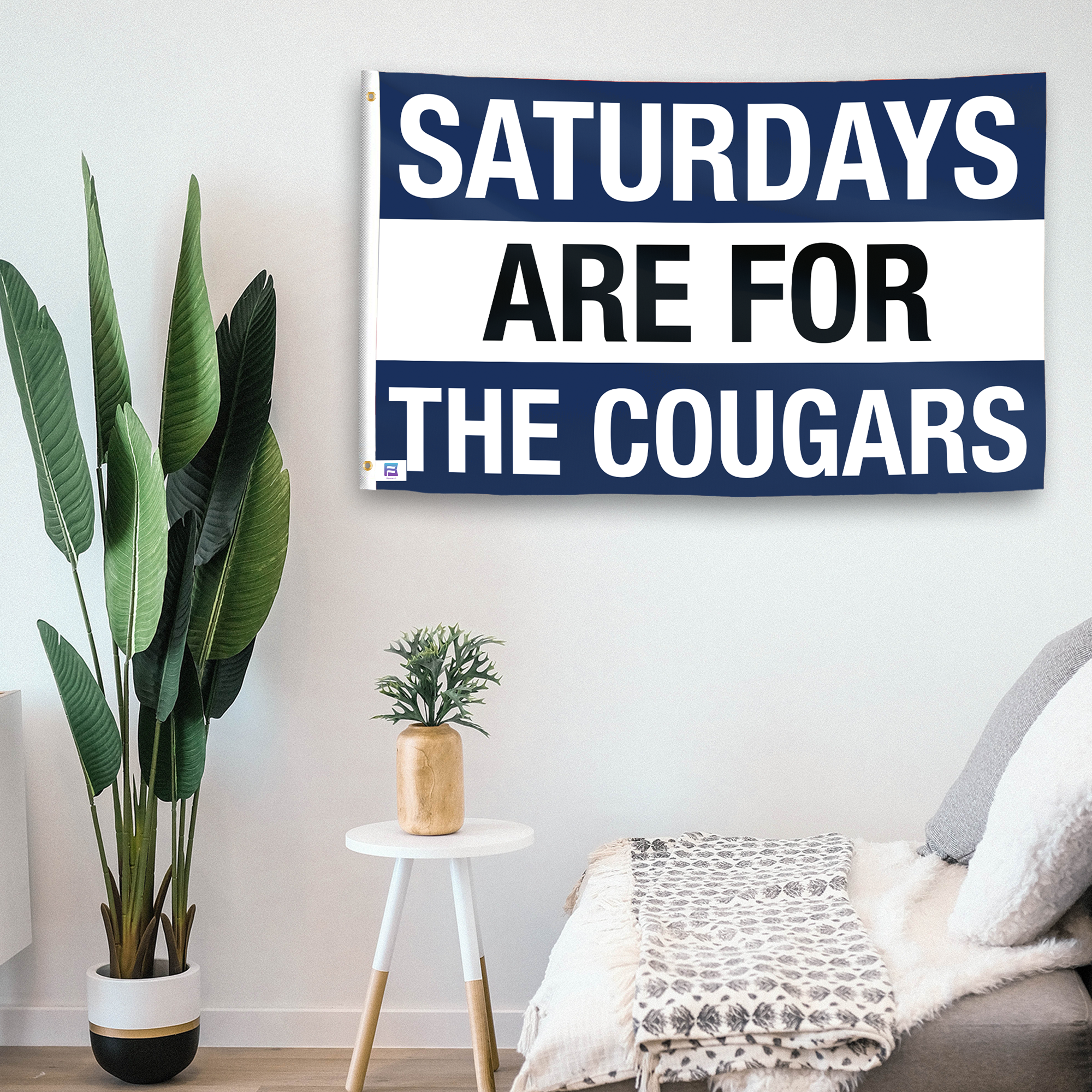 In a home setting, a flag with the saying "Saturdays Are for the Cougars BYU" is mounted on a white wall by a side table.